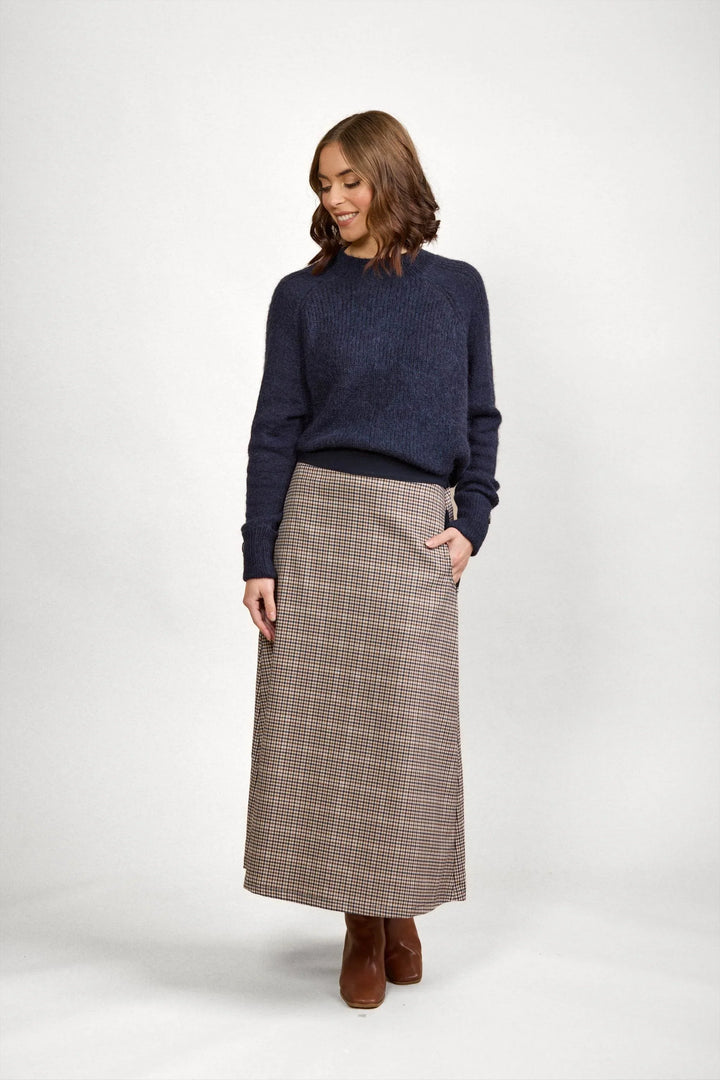 Woman wearing a navy knit sweater and checked maxi skirt with brown boots in studio