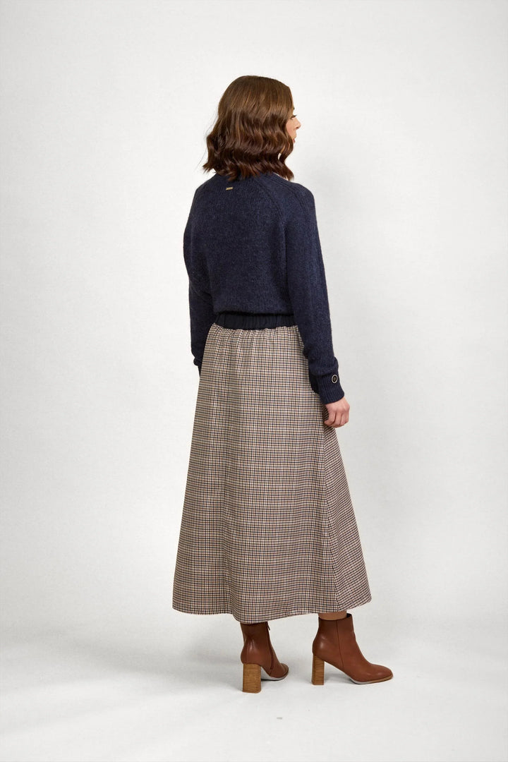 Woman in navy sweater and check midi skirt with brown heeled boots, facing backwards