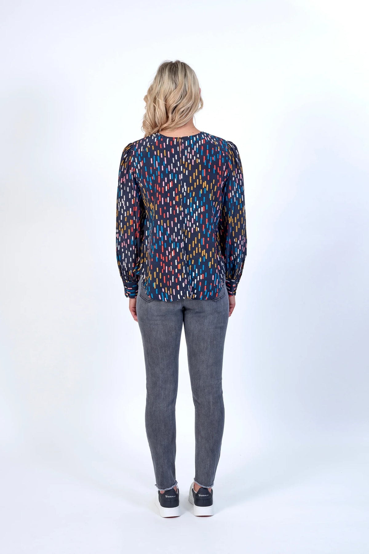Woman wearing a long sleeve patterned top and grey jeans, seen from the back