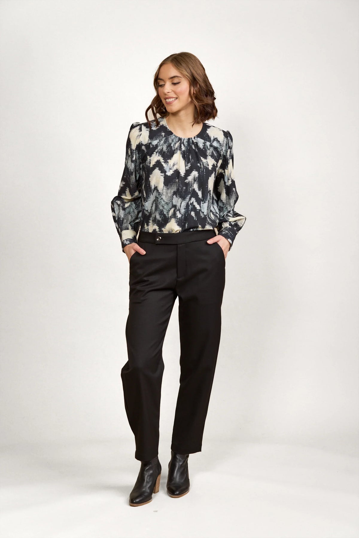 Woman wearing abstract patterned long sleeve blouse with black trousers and ankle boots