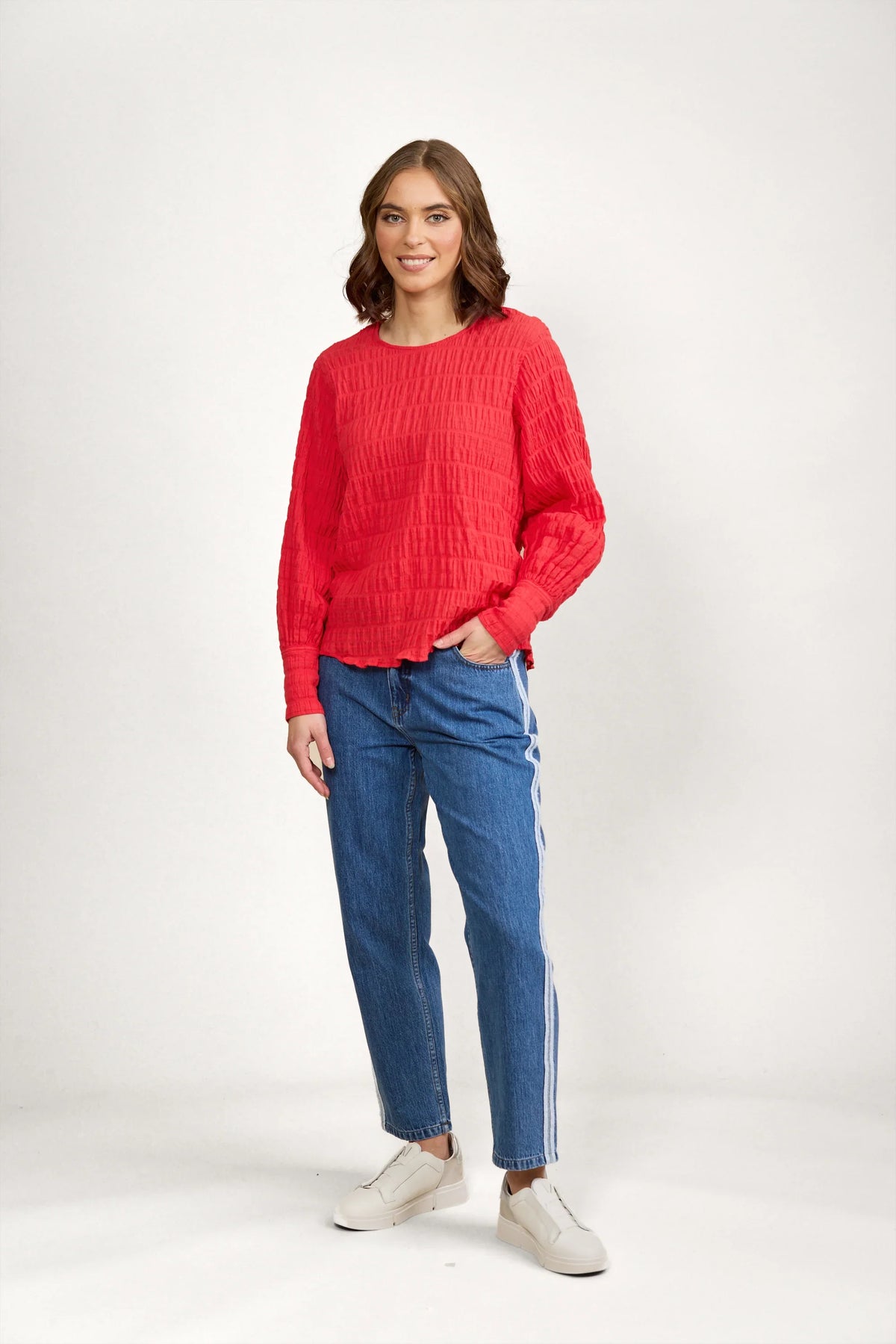Woman wearing a textured red long sleeve top with blue jeans and white sneakers