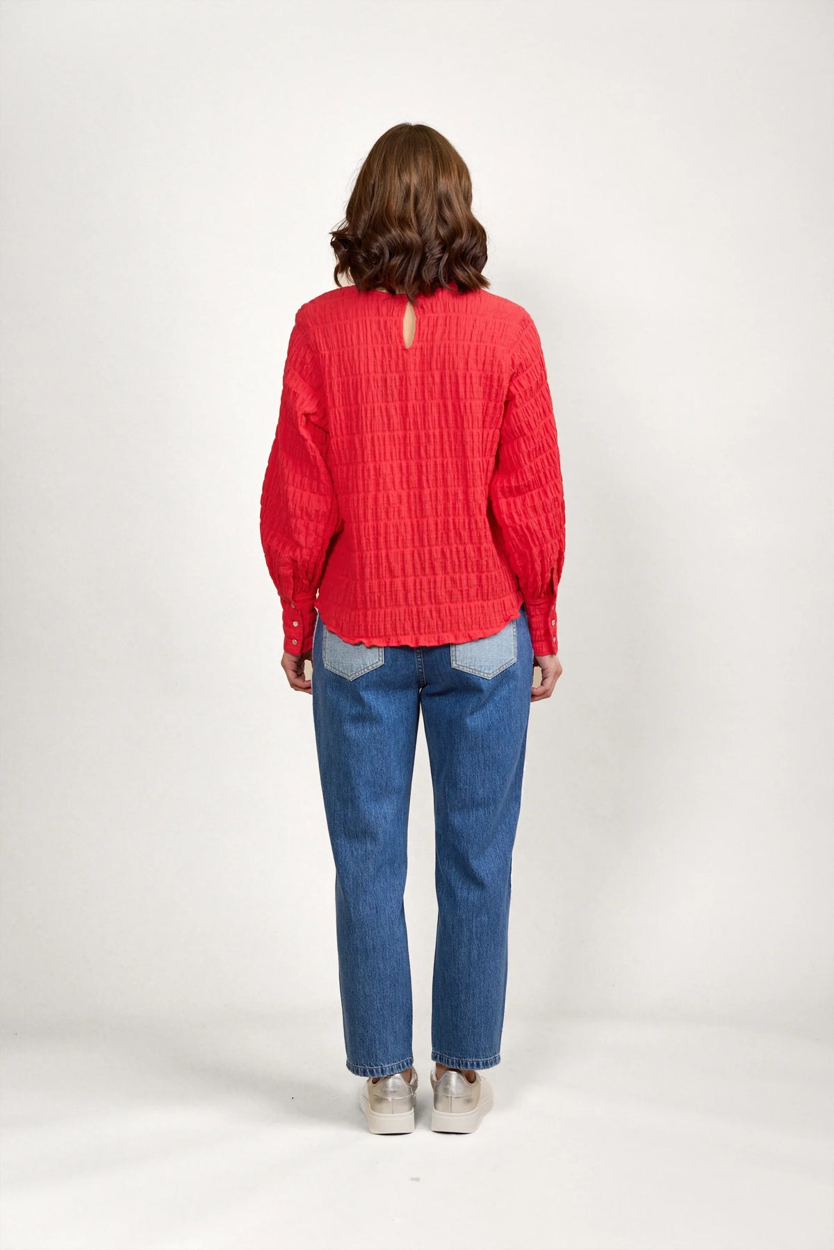 Woman wearing a textured red long-sleeve blouse and blue jeans, viewed from the back
