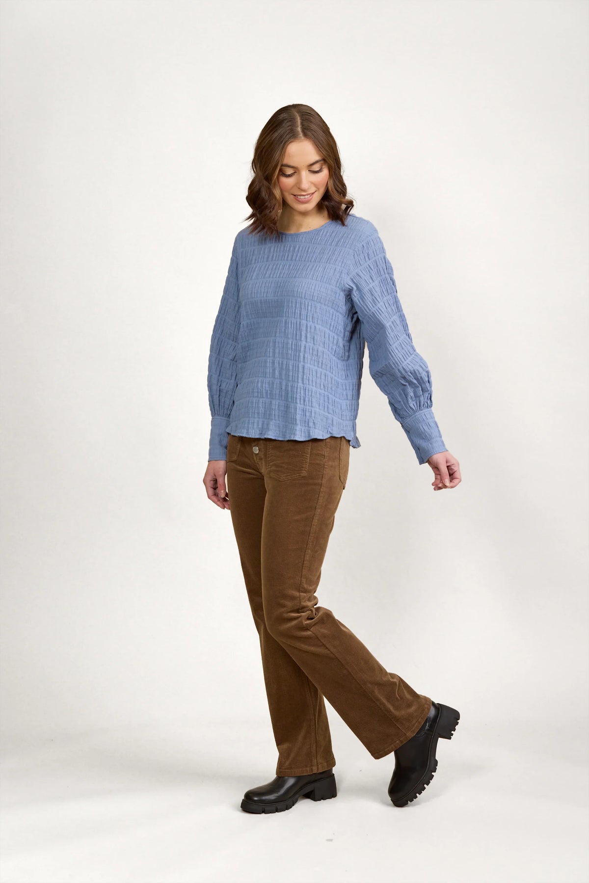 Woman wearing a textured blue volume top with long sleeves and brown corduroy pants
