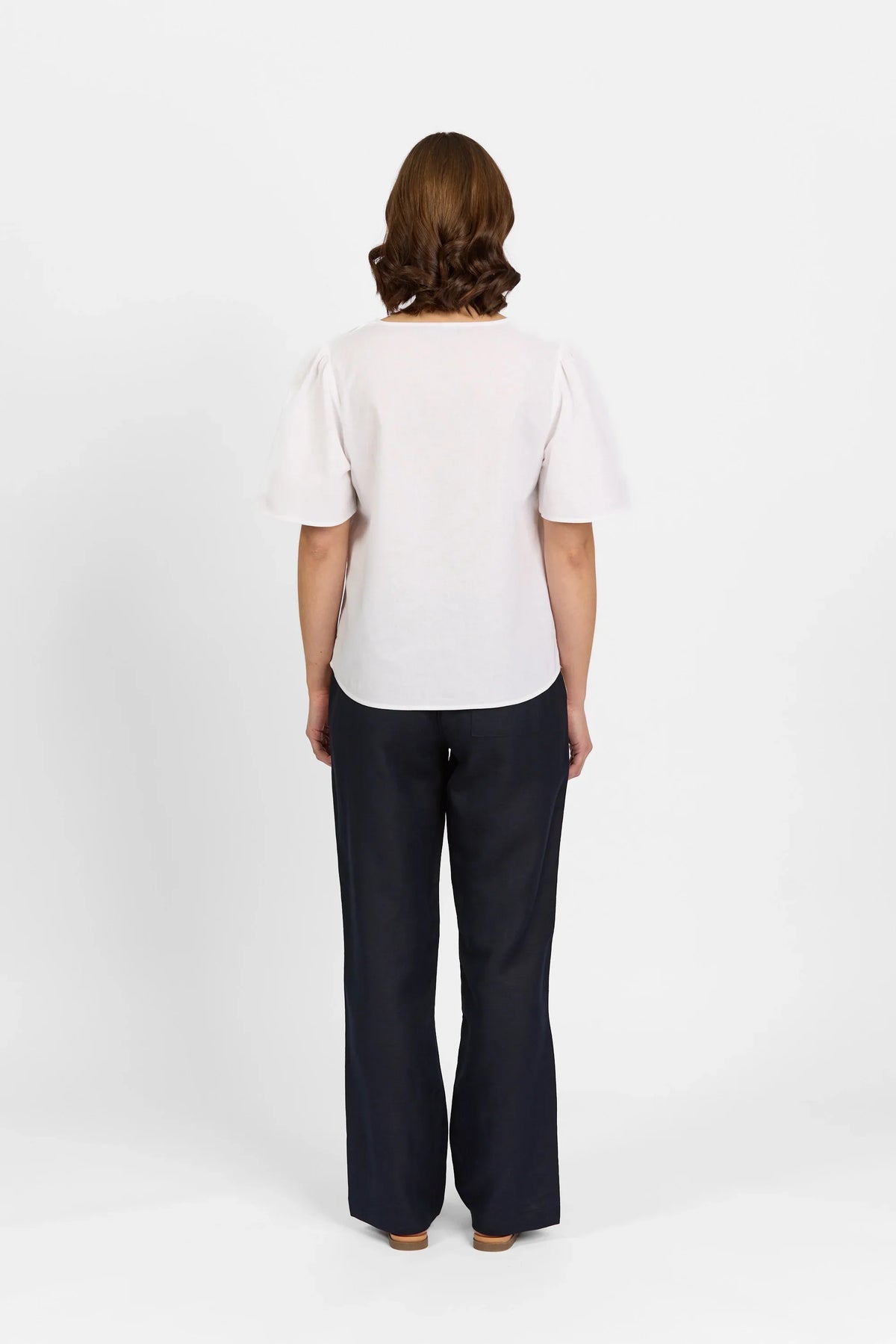 Woman wearing white short sleeve top and black wide leg pants, back view on white background