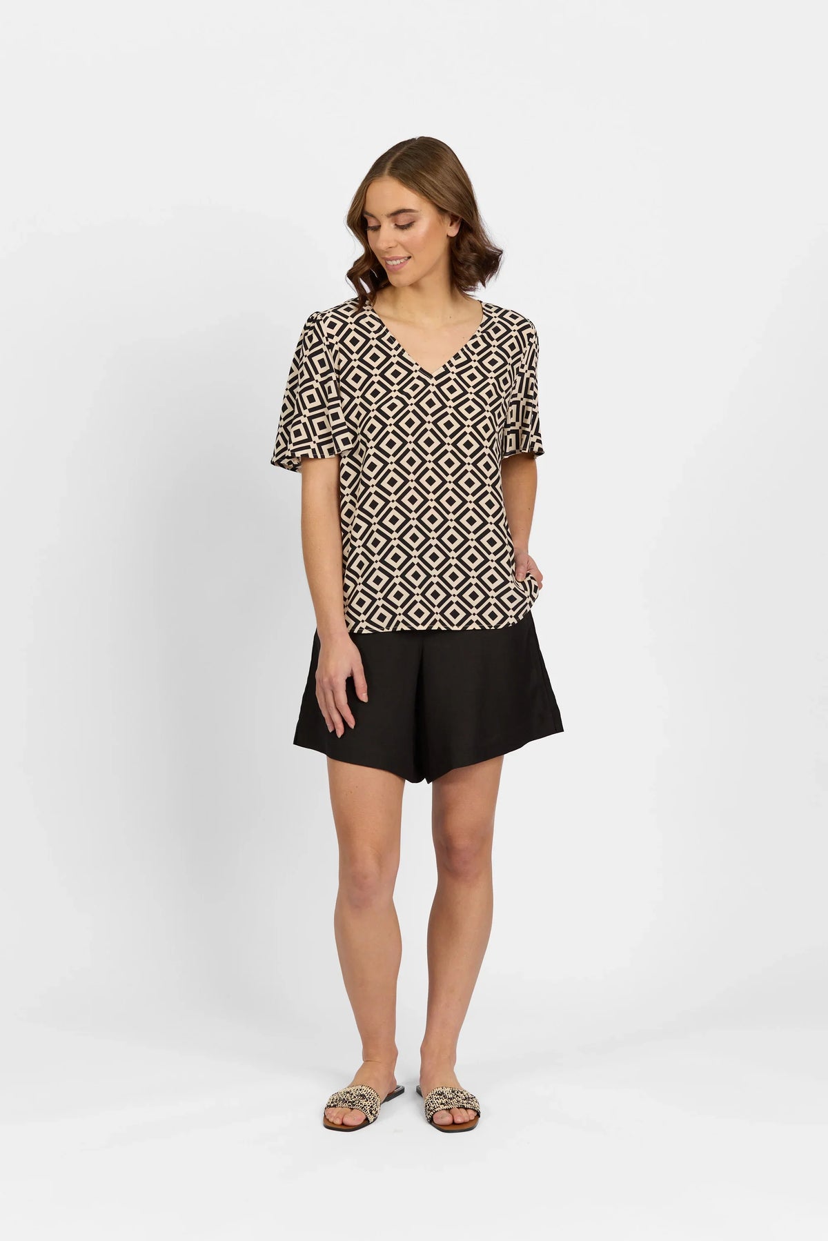 Woman wearing a geometric print V-neck top with short sleeves and black shorts, standing against a white background.