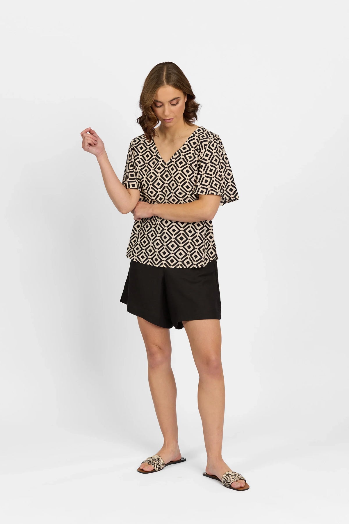 Woman wearing geometric print short sleeve top, black shorts, and woven slide sandals