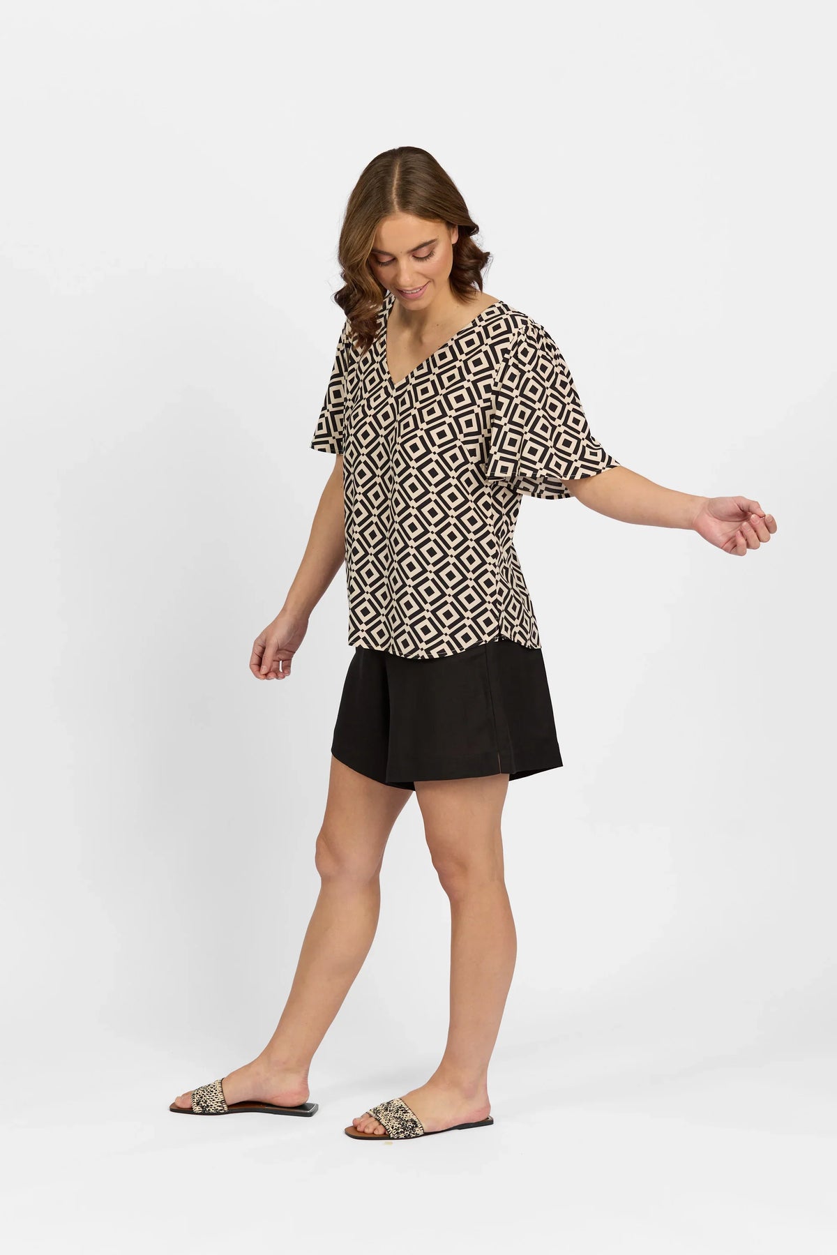Woman wearing geometric print short sleeve top with black shorts and slide sandals