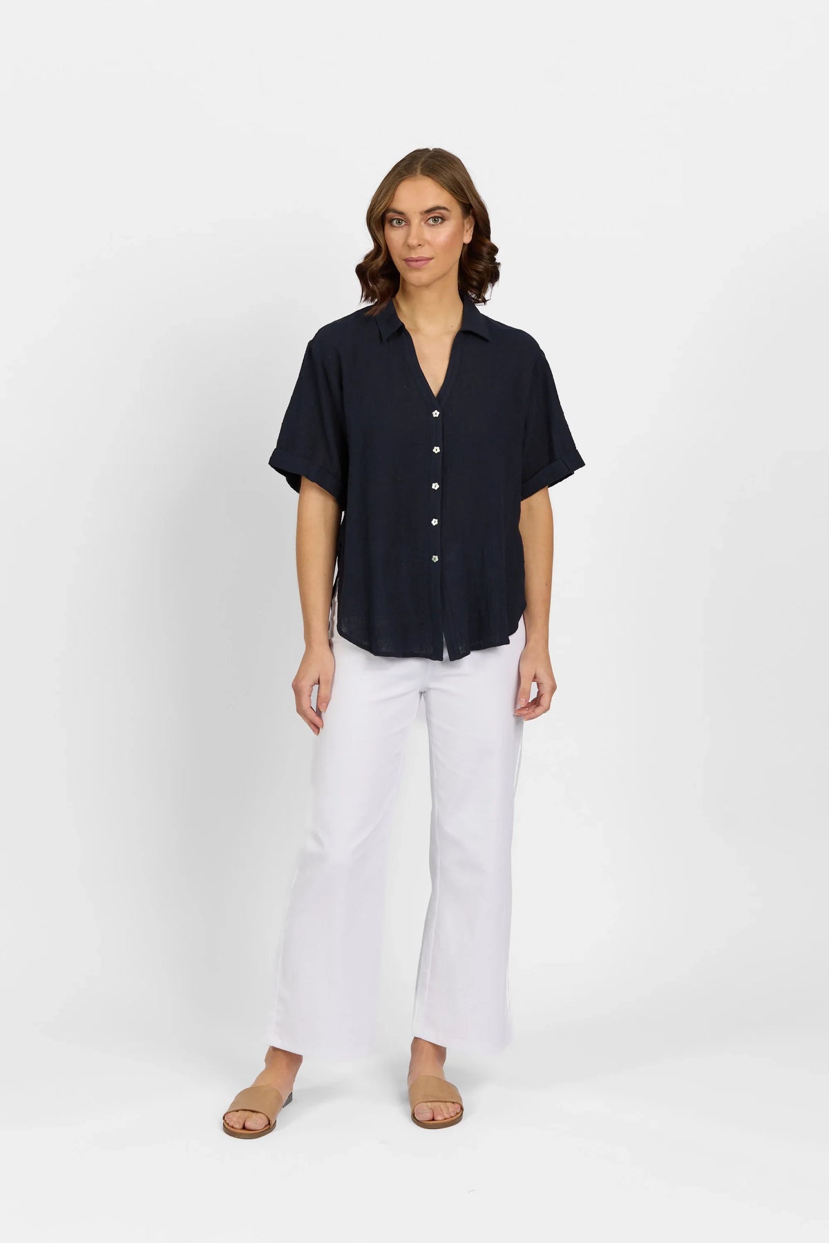 Woman wearing short sleeve navy button-up shirt and white flare pants, studio background