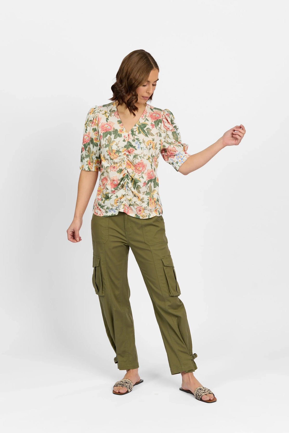 Woman wearing a floral v-neck blouse with puff sleeves and olive cargo pants against white background.