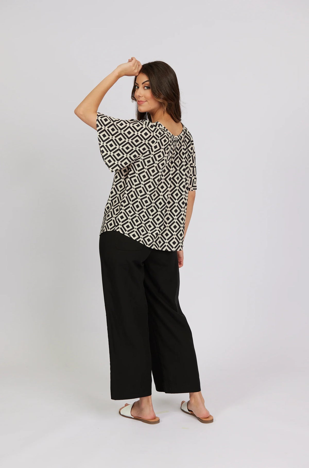 Woman wearing a geometric patterned top with black wide-leg pants and white sandals