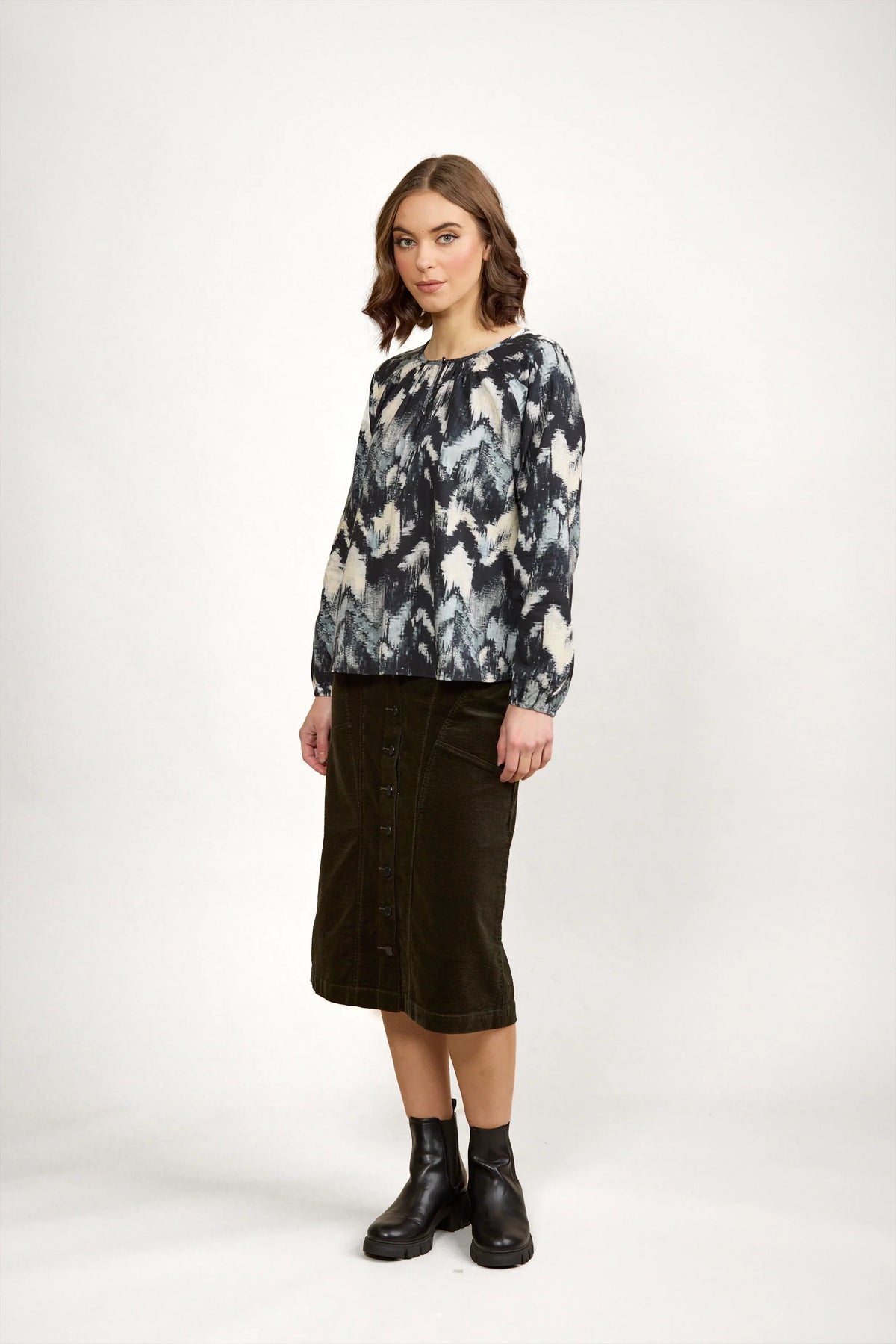 Woman wearing abstract print long sleeve blouse, olive button-front midi skirt, black boots