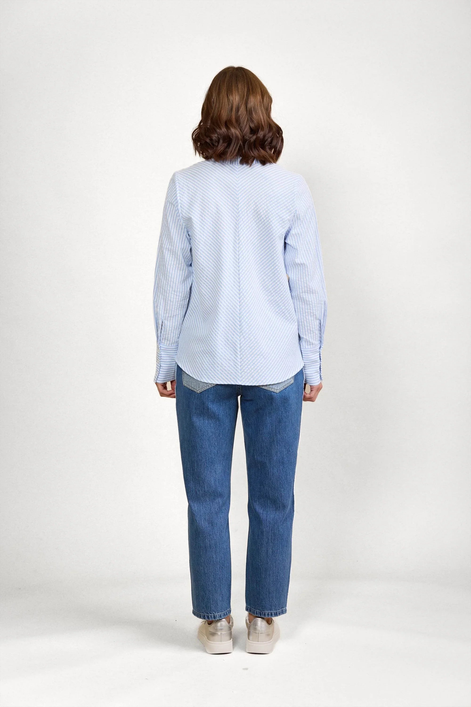 Woman wearing blue and white striped long sleeve shirt and straight leg jeans, back view