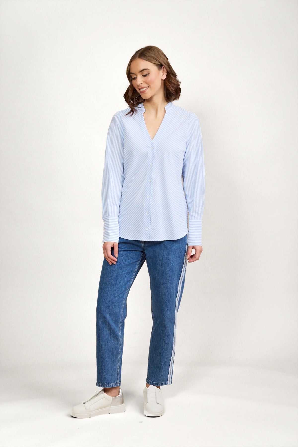 Woman wearing blue and white striped button-up shirt, jeans, and white sneakers