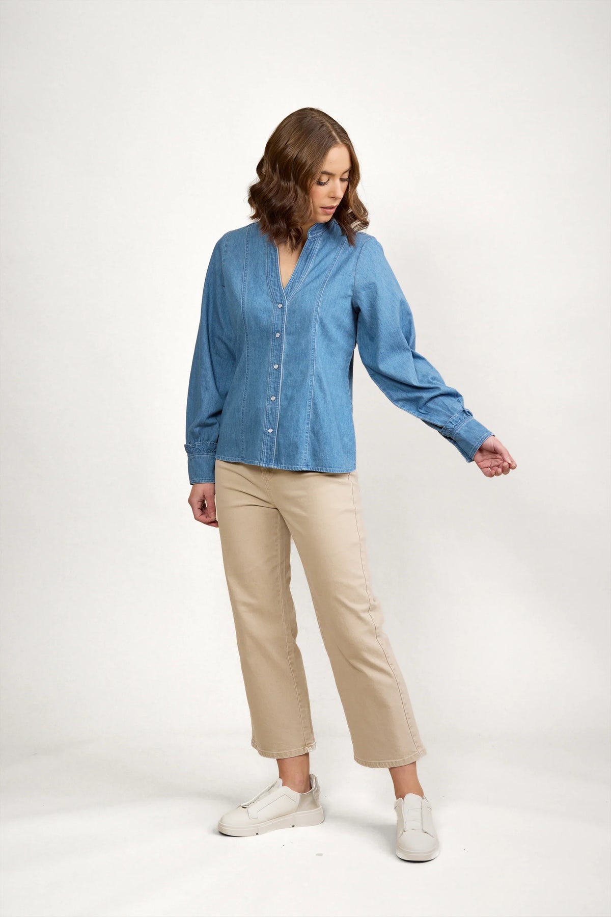 Woman modeling a blue denim shirt with button front and long sleeves, paired with beige pants