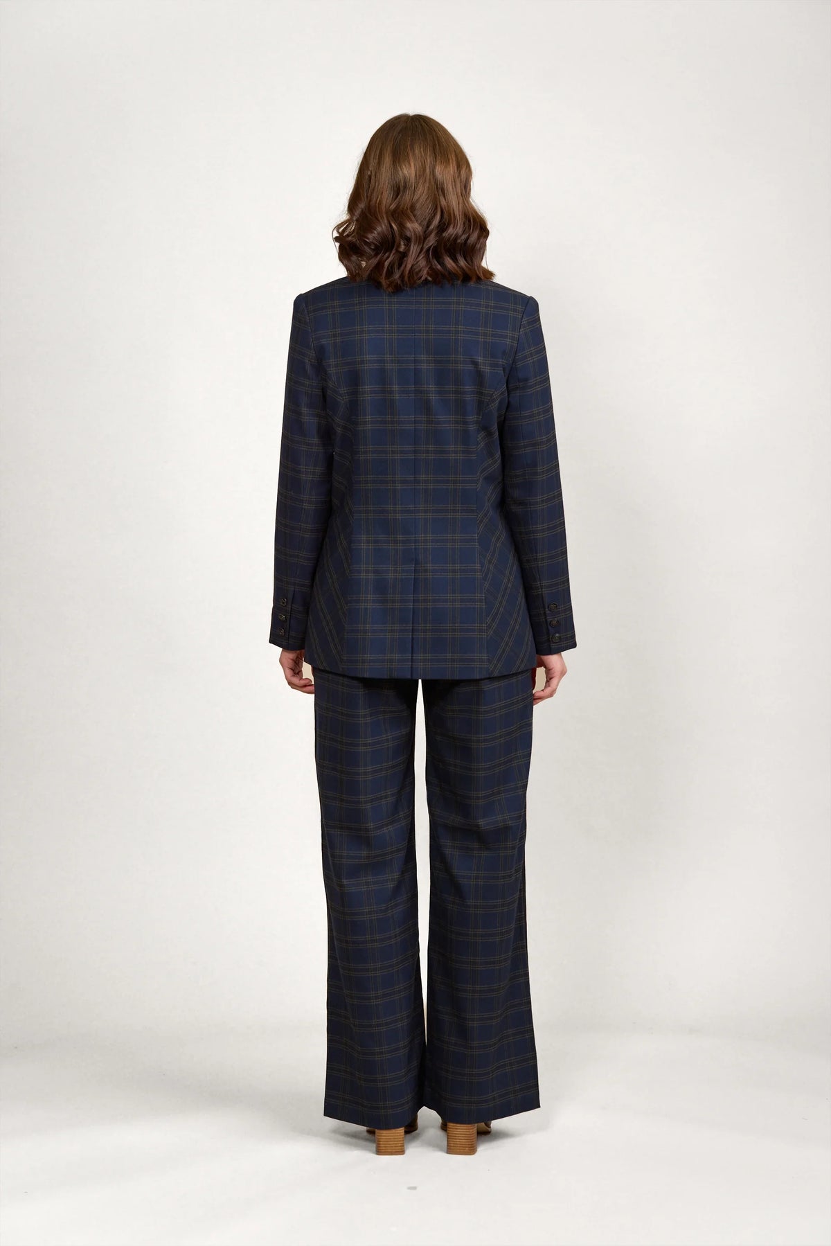 Back view of woman in navy check plaid blazer and wide-leg pants, studio background