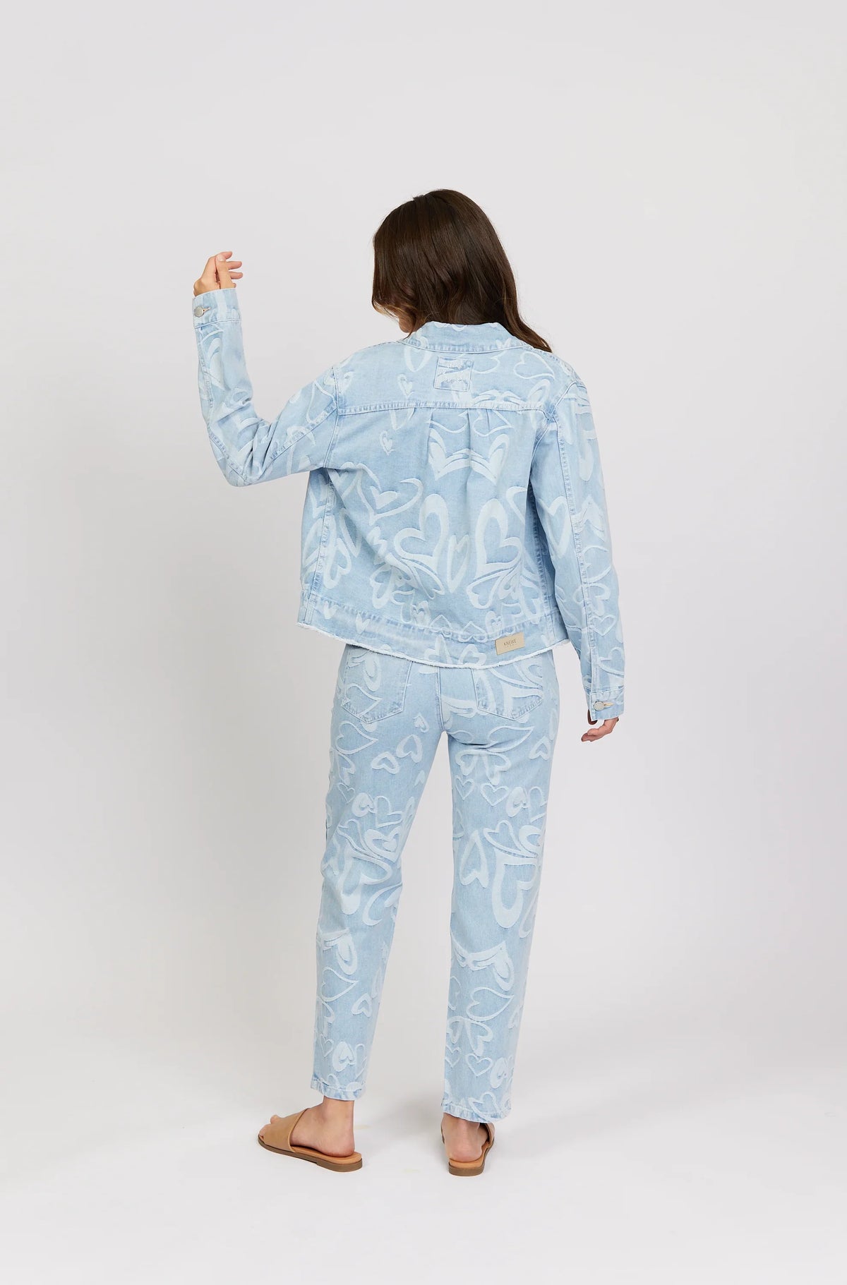Woman wearing light blue denim jacket and jeans with white heart patterns, back view