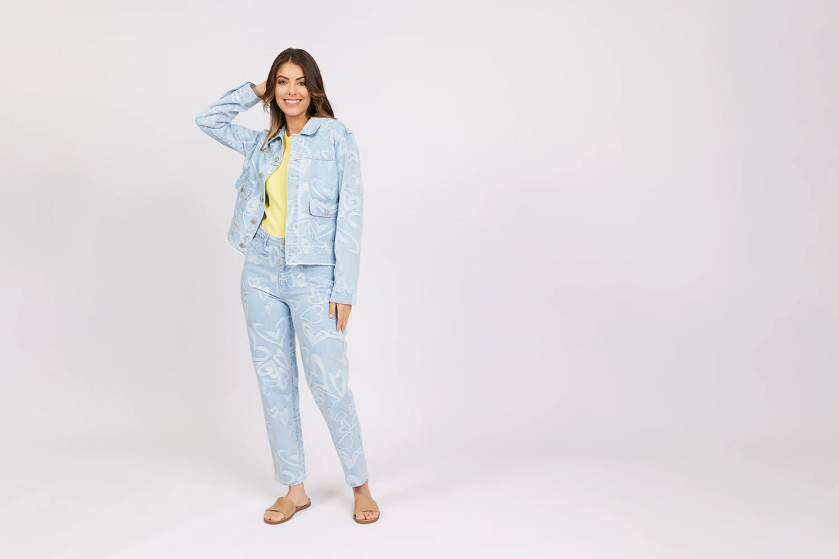 Woman modeling light blue denim jacket and jeans with white heart patterns, yellow top, sandals