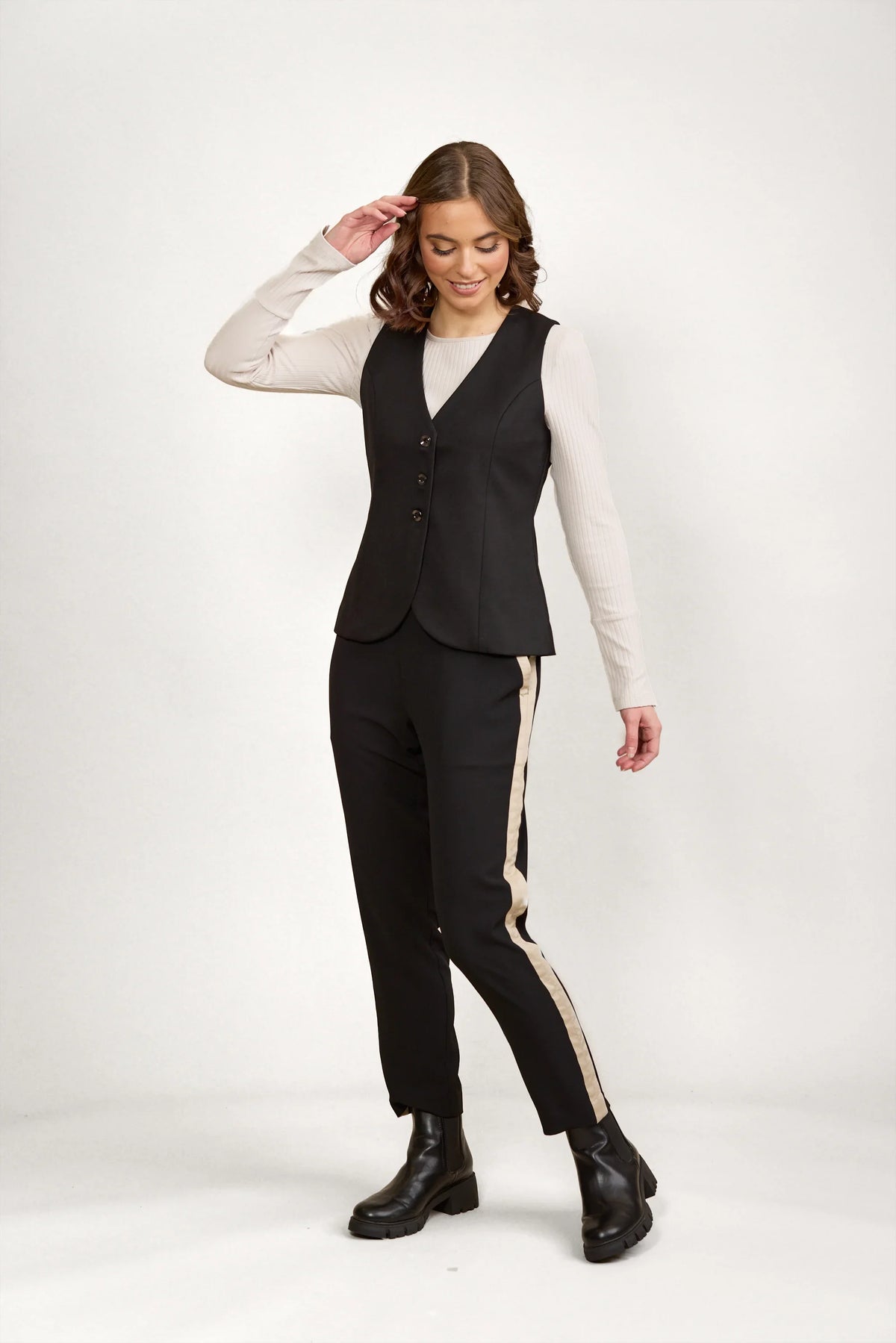 Woman wearing black tailored vest, striped trousers, and black boots on neutral background