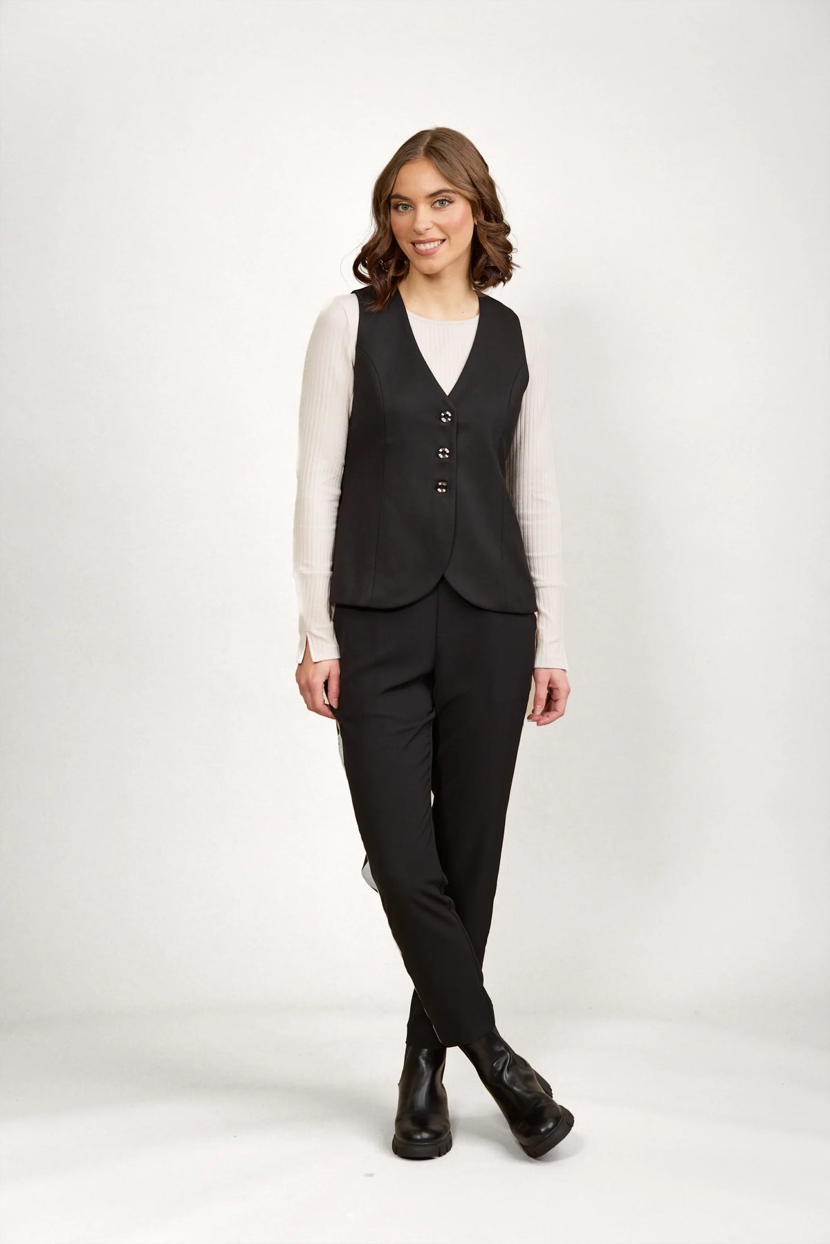 Woman wearing black tailored vest and pants set with a white ribbed long sleeve top