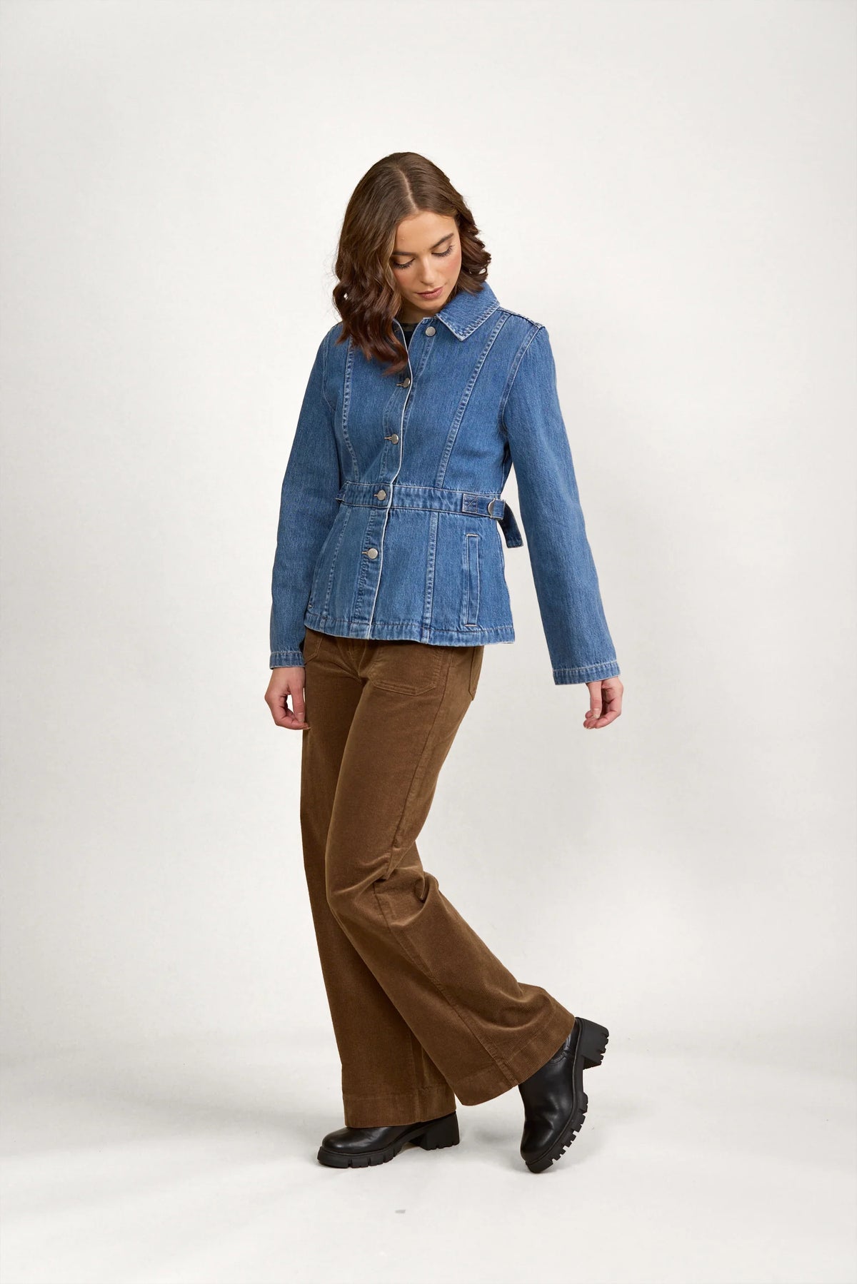 Woman wearing a fitted blue denim jacket with brown corduroy pants and black boots