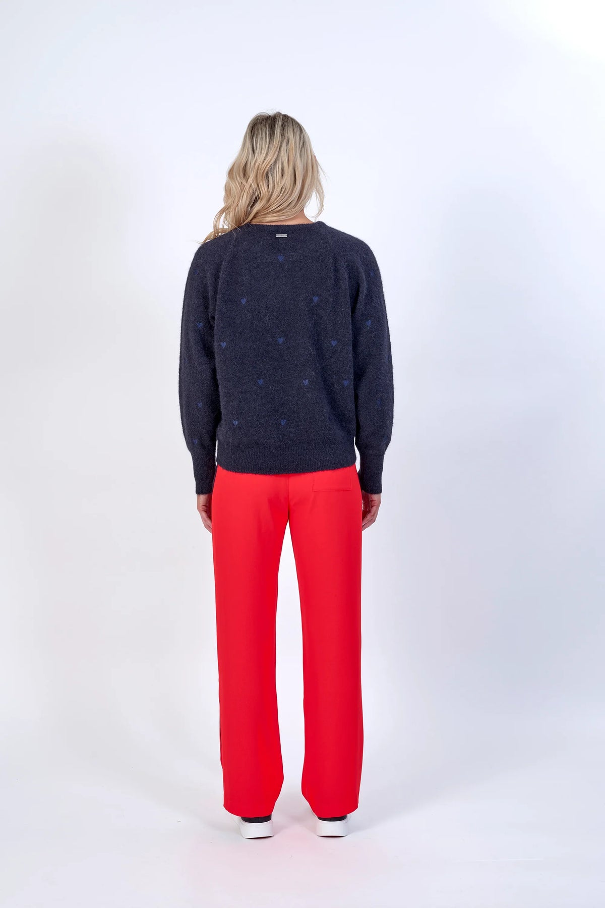 Woman wearing bright orange wide-leg pants and a dark sweater, back view, studio setting