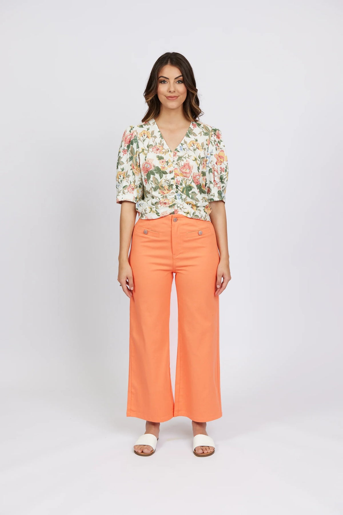 Woman wearing apricot wide-leg jeans, floral blouse, and white sandals, front view