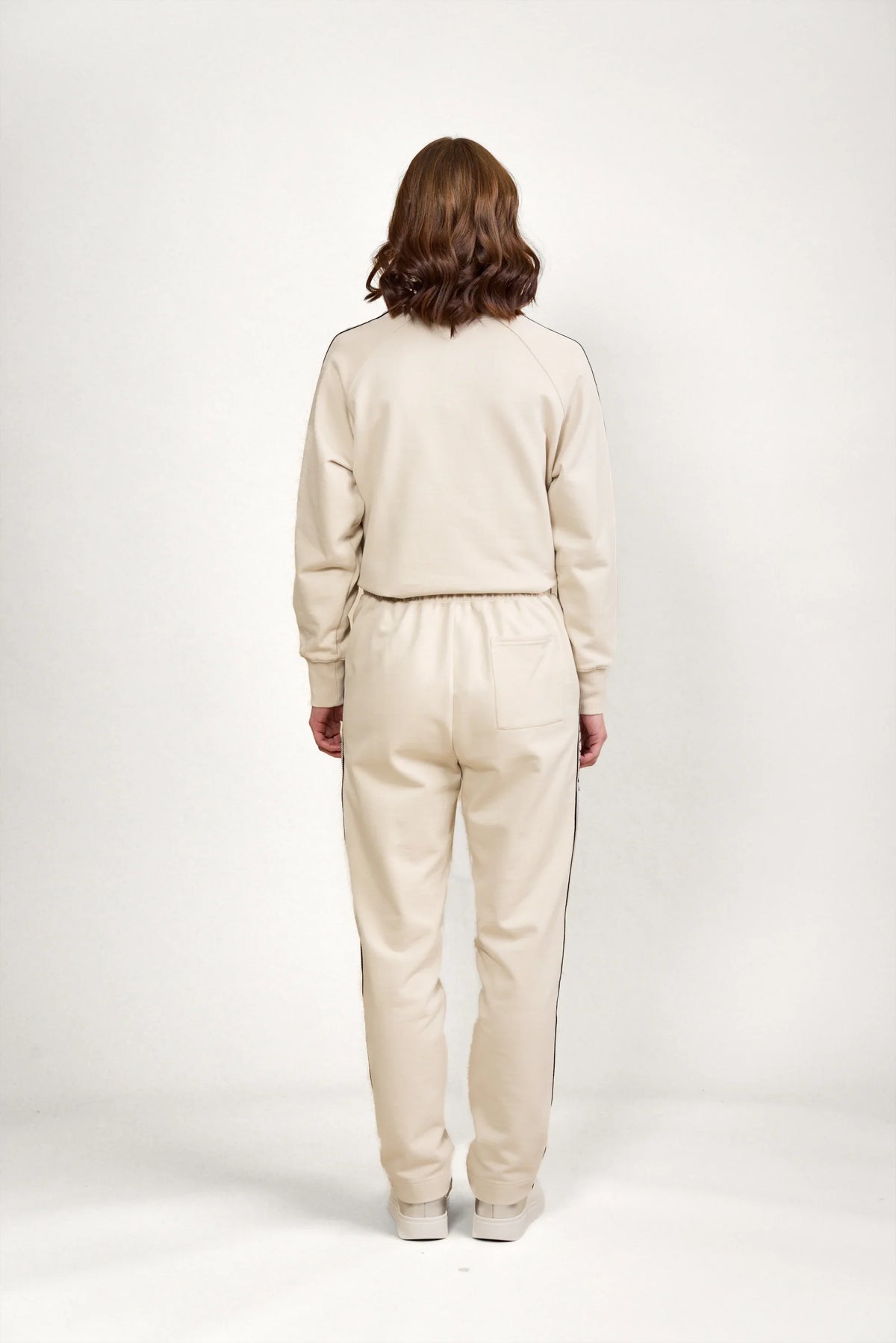 Back view of woman wearing stone-colored jogger pants and sweatshirt with black side piping
