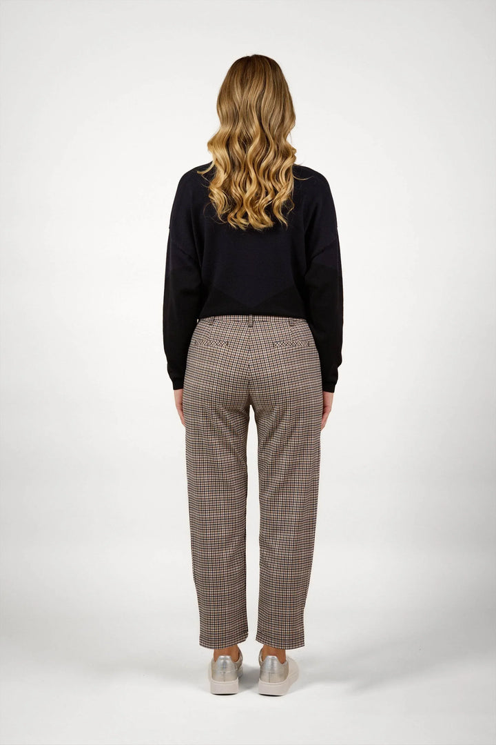 Woman wearing checkered straight-leg pants and black sweater, back view, studio setting
