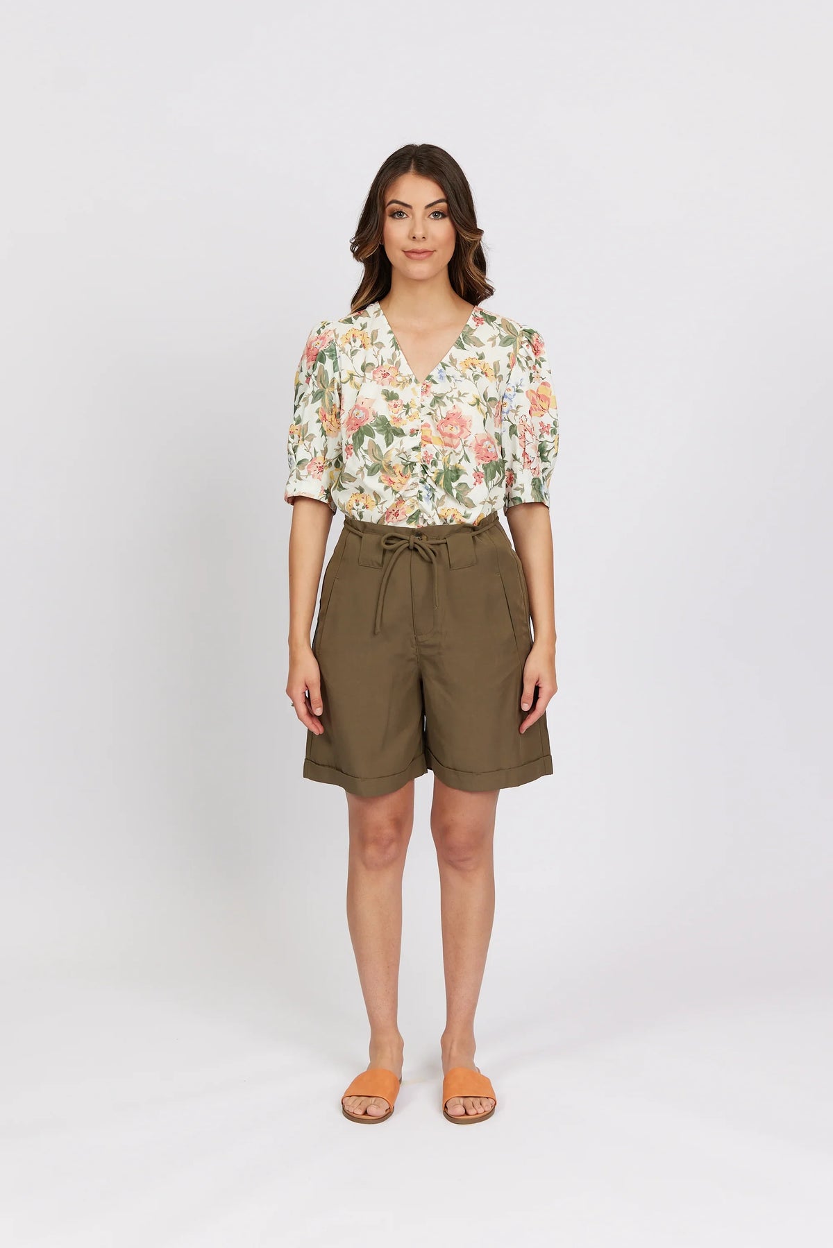 Woman wearing khaki high-waisted shorts and a floral blouse with short sleeves.