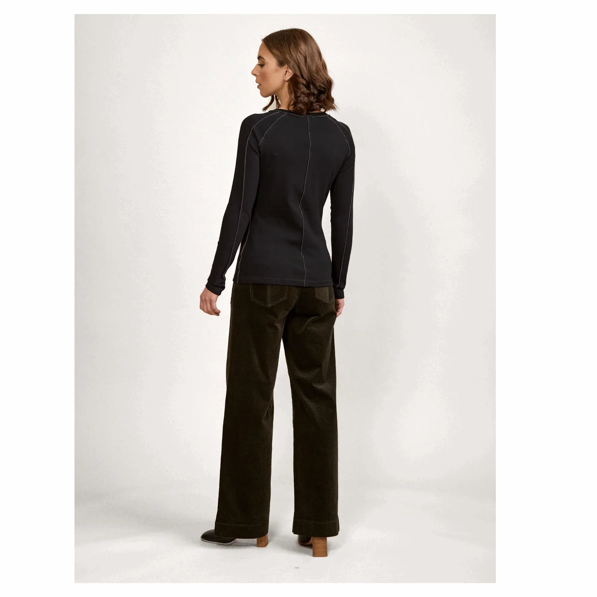 Woman in black long-sleeve top and wide-leg dark pants, shown from the back, studio setting