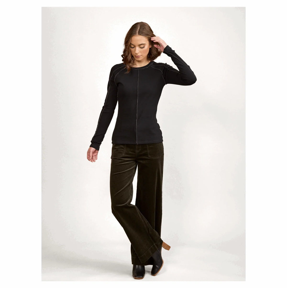 Woman wearing black long sleeve top and wide leg brown corduroy pants, fashion studio shot