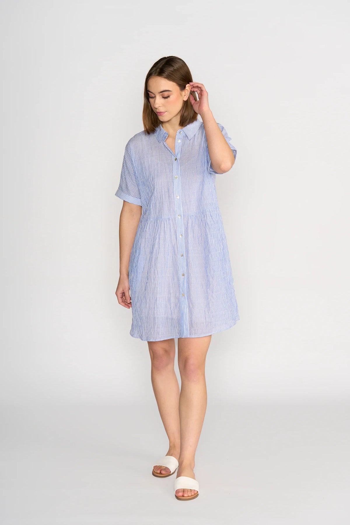 Woman wearing a short-sleeve blue striped button-up cocoon dress, standing indoors.