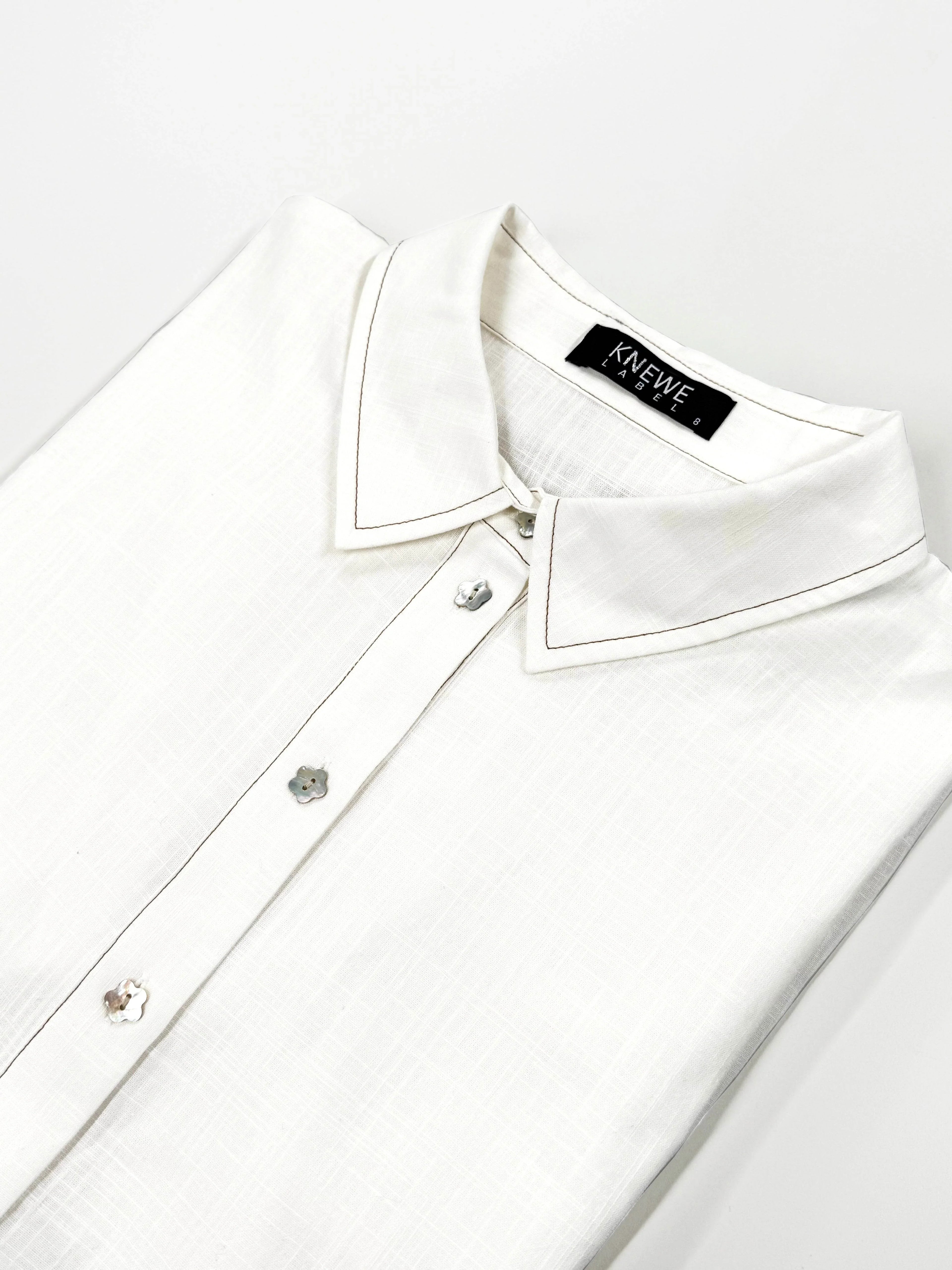 Folded off-white cocoon dress shirt with floral buttons and pointed collar on white background