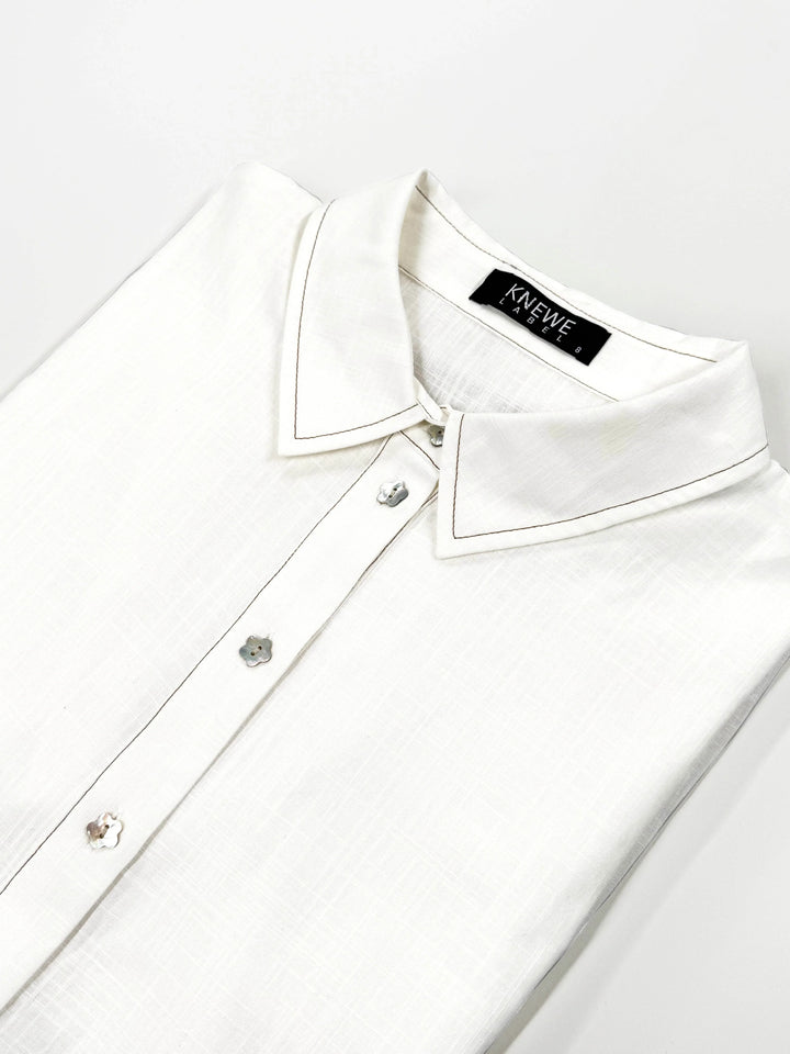 Folded off-white cocoon dress shirt with floral buttons and pointed collar on white background