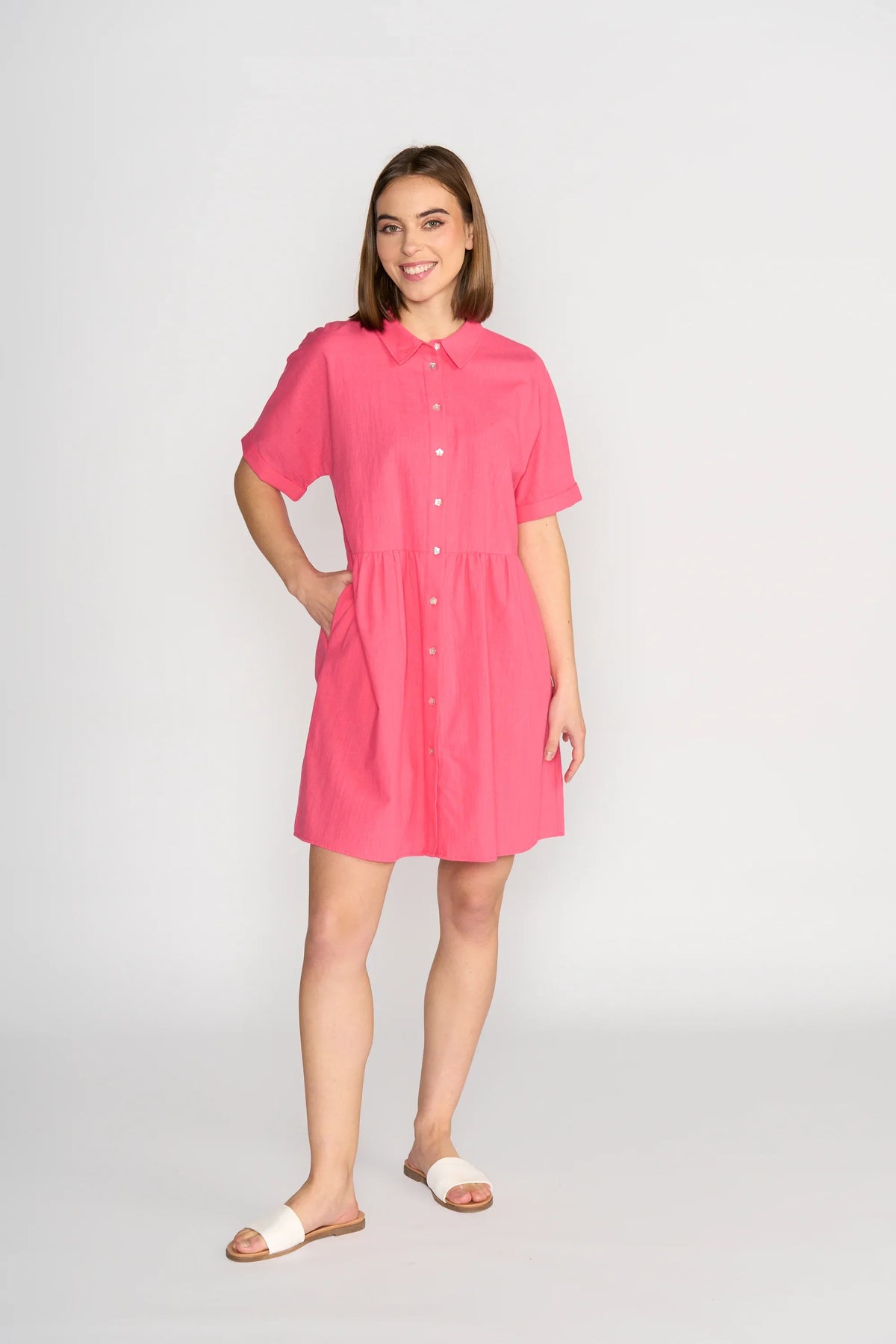 Woman wearing short-sleeve raspberry pink cocoon dress with buttons, standing in studio
