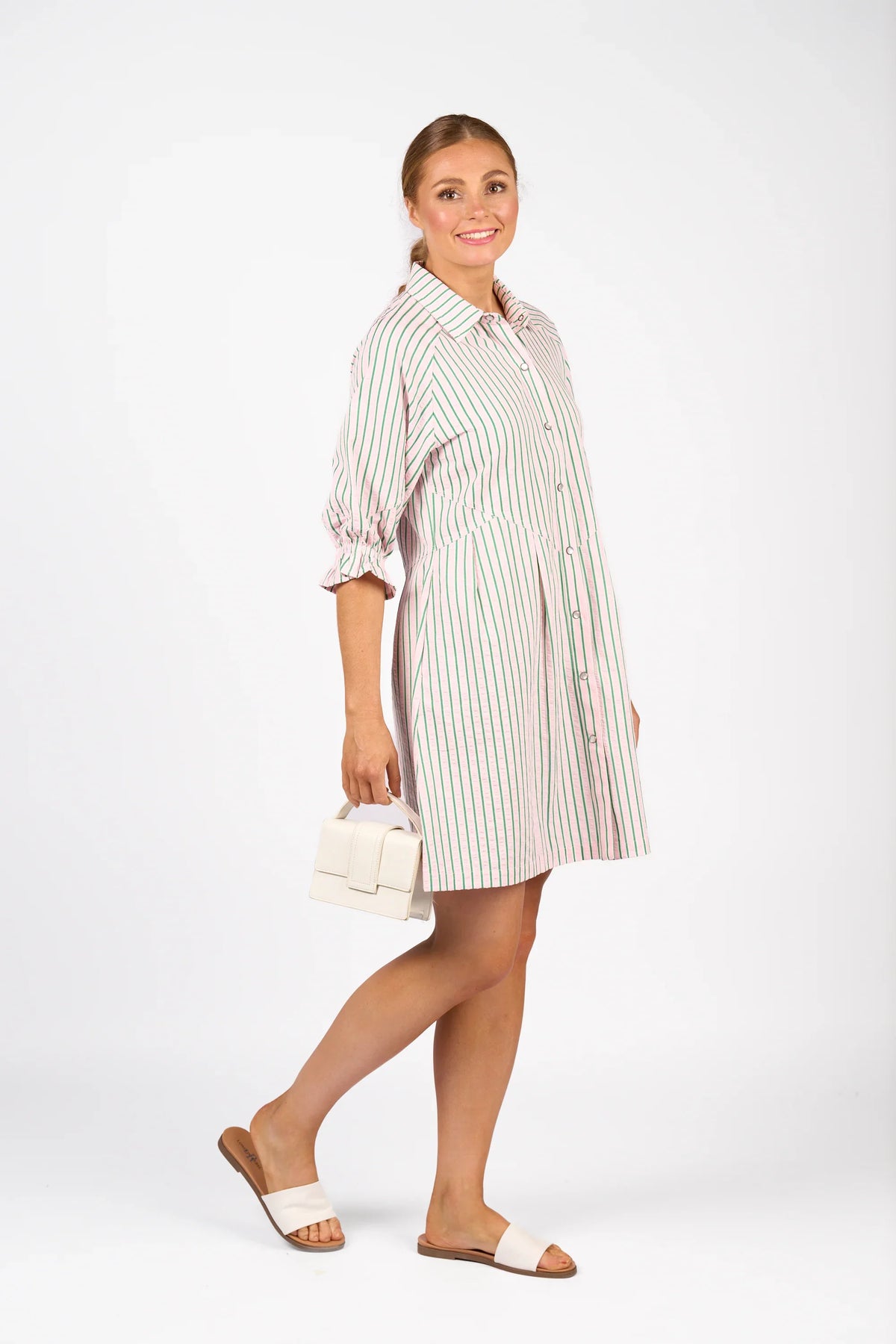 Woman in a striped button-up shirt dress with puff sleeves, holding a white handbag