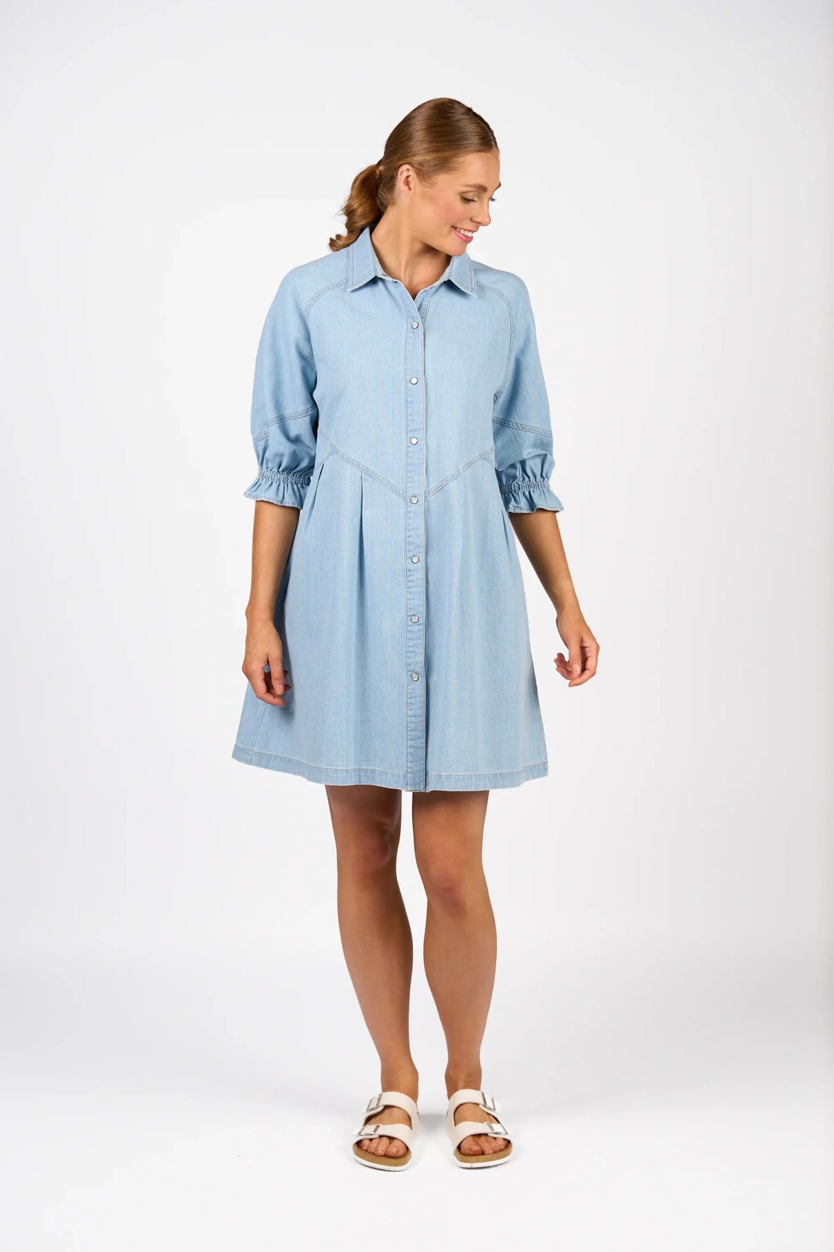 Woman wearing light wash denim shirt dress with three-quarter sleeves and white sandals