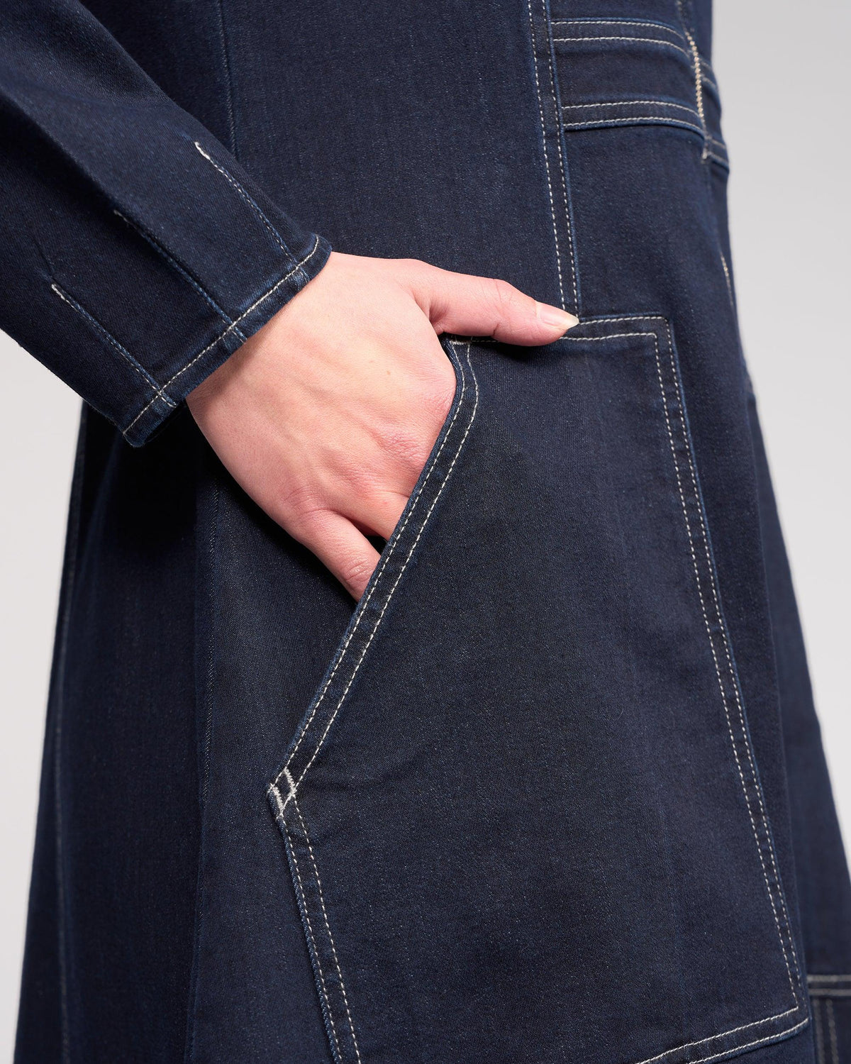 Close-up of a hand in the large front pocket of the Knewe Label Phoenix Dress in Ink Denim, featuring visible white stitching and a hint of long sleeve.