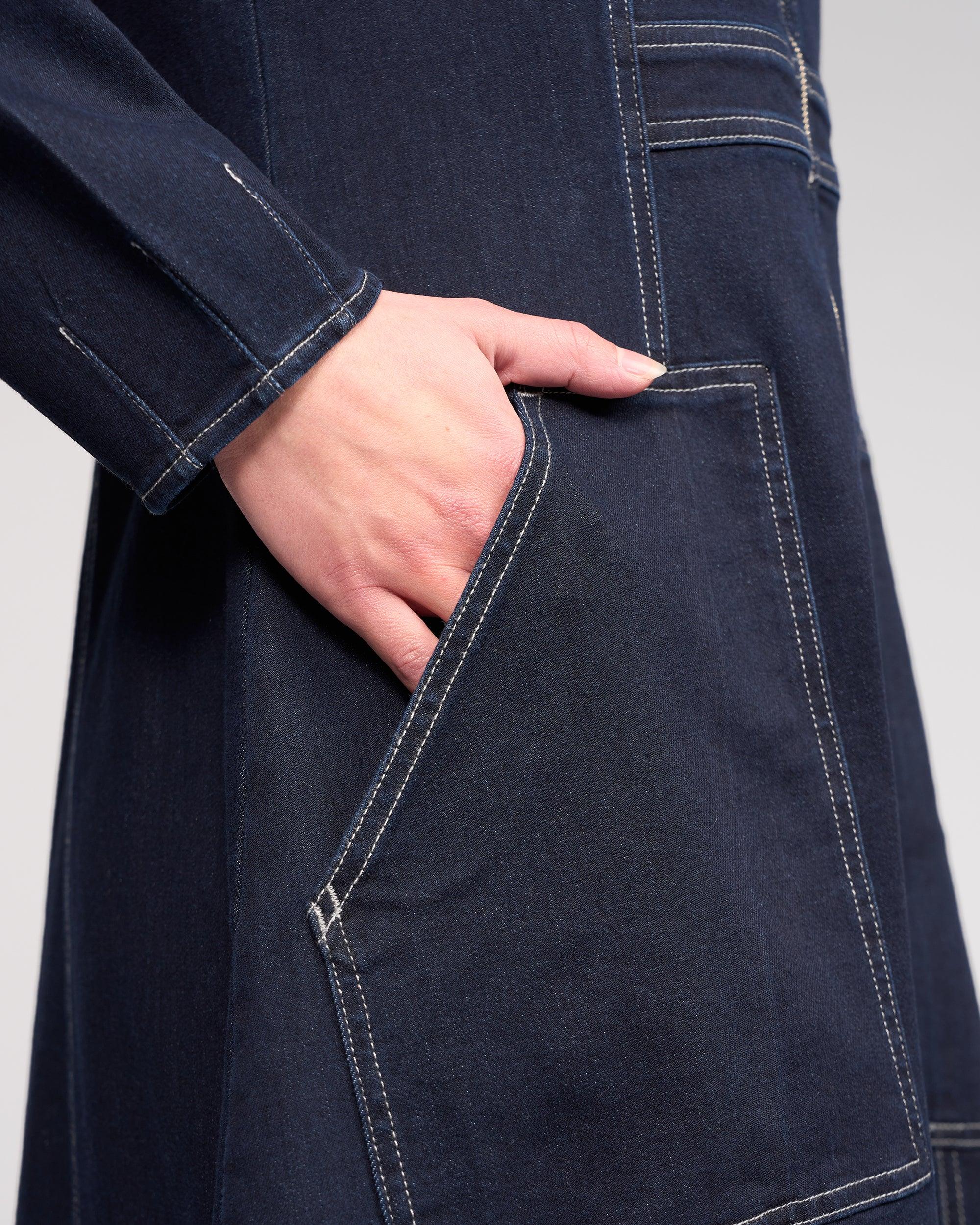 Close-up of a hand in the large front pocket of the Knewe Label Phoenix Dress in Ink Denim, featuring visible white stitching and a hint of long sleeve.