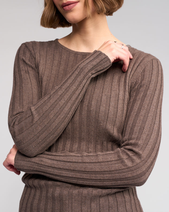 A woman with a short bob wears the Felix Sweater - Truffle by Knewe Label, a long sleeve ribbed knit, standing with arms crossed. Only her torso and part of her face are visible against a plain background.