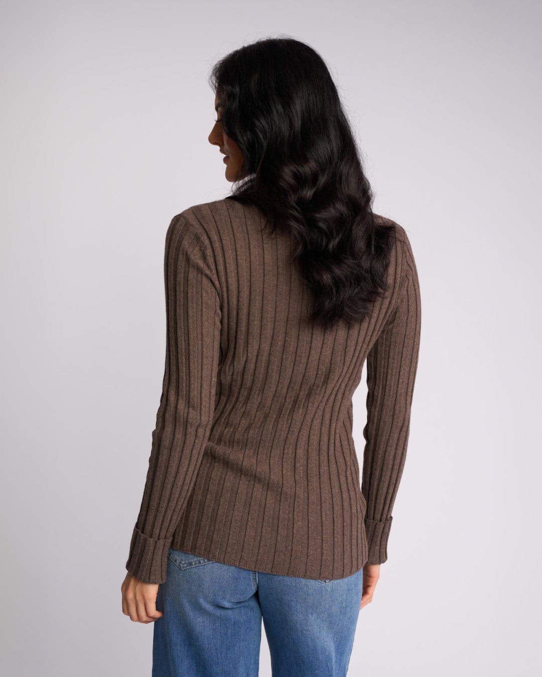 Back view of a woman wearing the Knewe Label Felix Cuffed Sweater in Truffle and blue jeans.
