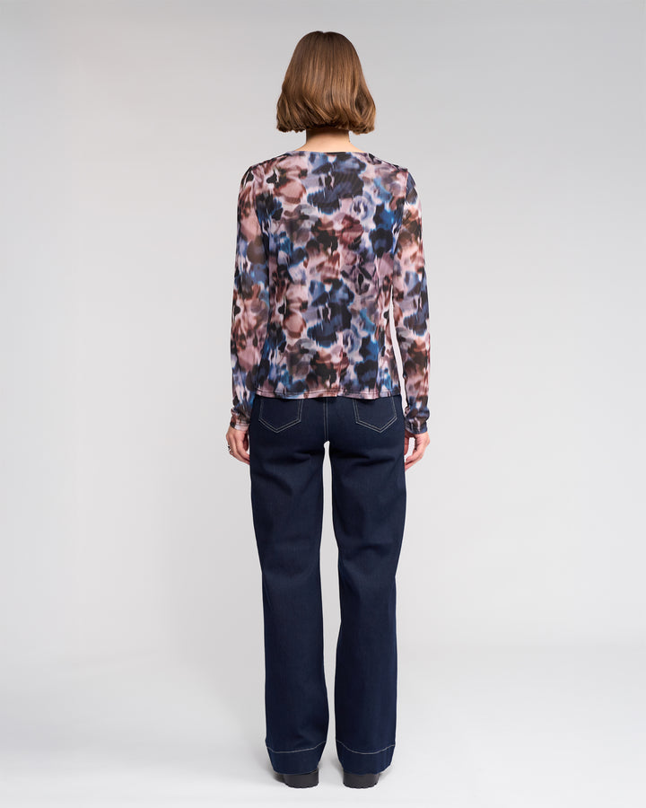 A person with short brown hair, seen from behind, wears the Apex Top - Celine by Knewe Label and high-waisted wide-leg dark blue jeans with white stitching, standing against a plain light background.