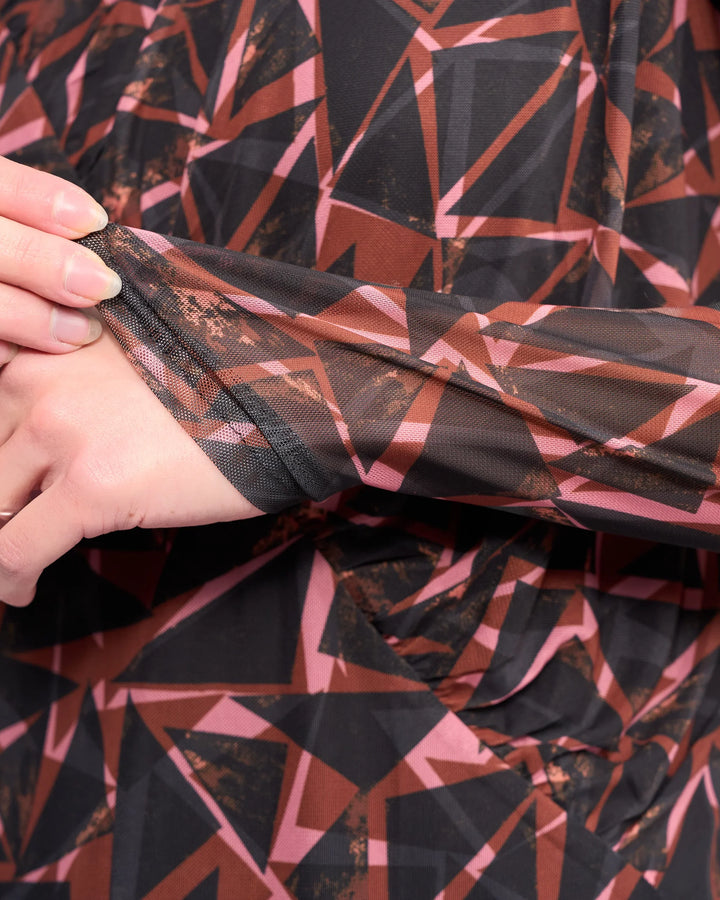 A close-up of a hand gently pulling the sleeve of Knewe Label's Apex Top - Dusk, a long sleeve mesh top in black, brown, and pink geometric print with soft, textured fabric.