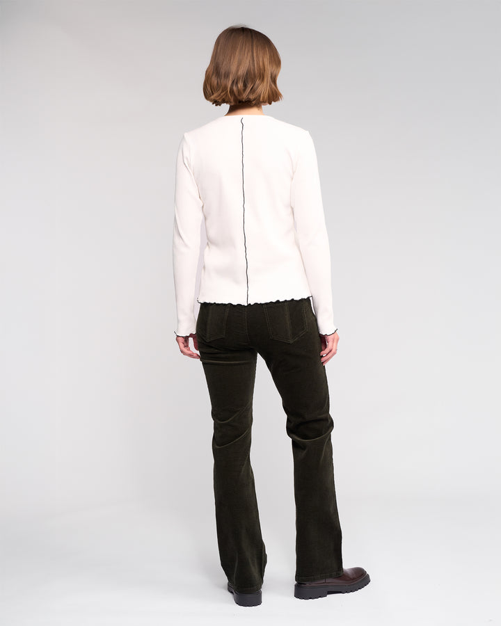 A person with short hair, seen from behind, wears the Knewe Label Sofie Top in Off White—a long sleeve ribbed cotton top with a central seam—paired with black pants against a plain light background.