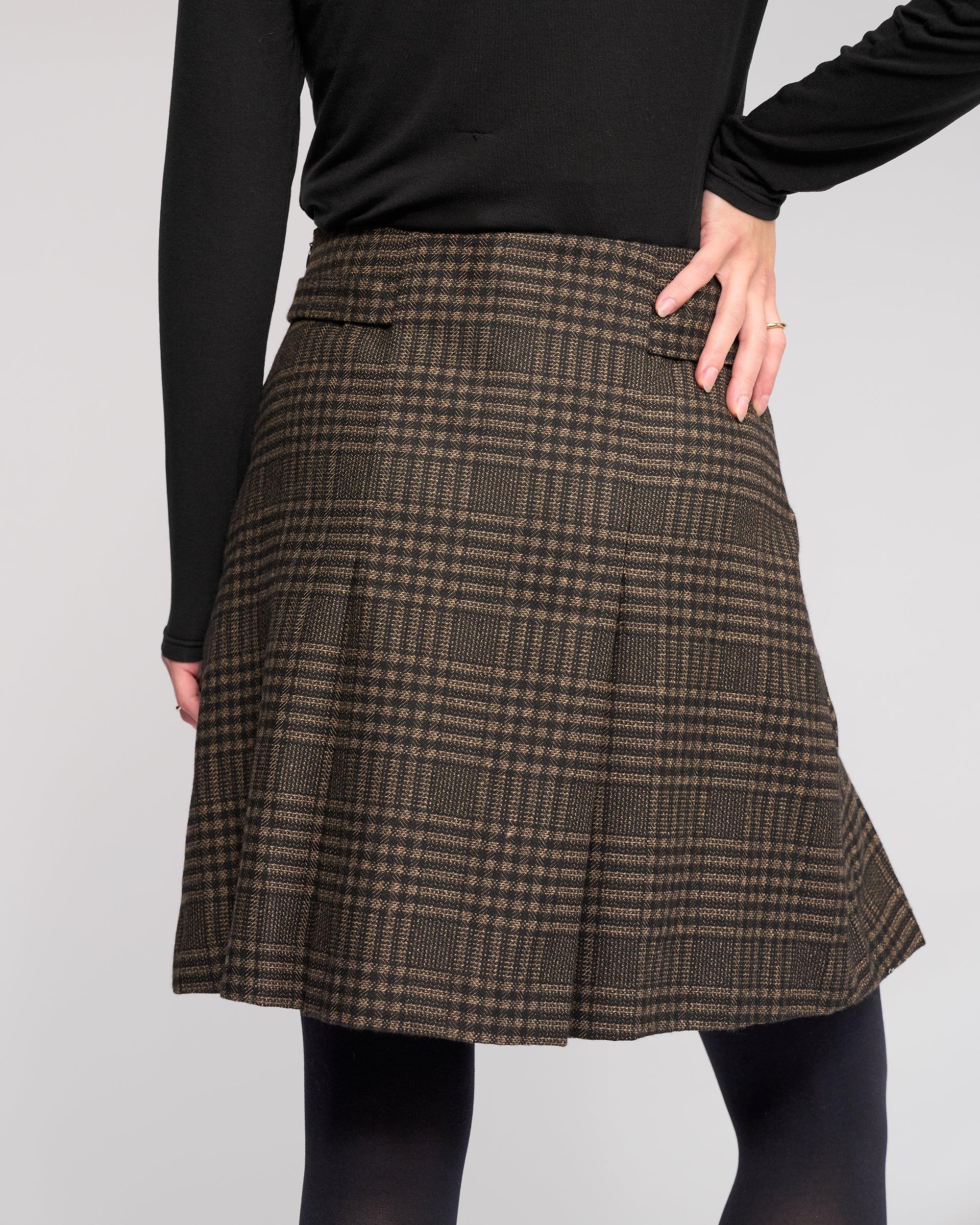 A person wears the Knewe Label Soho Skirt - Check with a black long-sleeve top, posing hand on hip against a plain background. Only their body from shoulders to knees is shown.