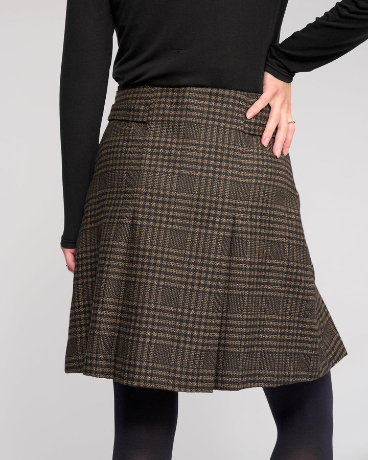 A person wears the Knewe Label Soho Skirt - Check with a black long-sleeve top, posing hand on hip against a plain background. Only their body from shoulders to knees is shown.