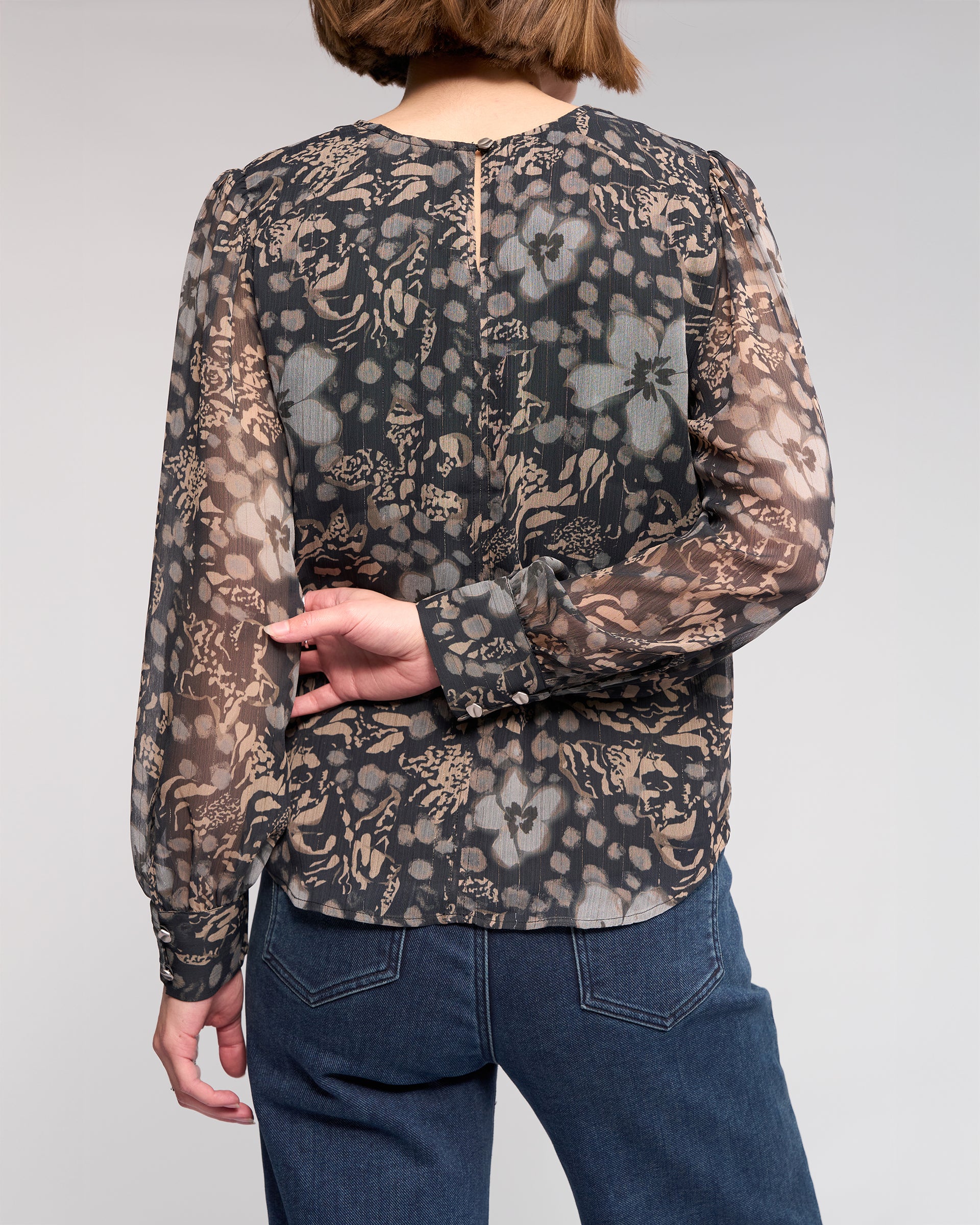A person stands with their back to the camera, wearing the Knewe Label Lexie Top - Hazy and blue jeans. One hand is behind their back, resting on their side.