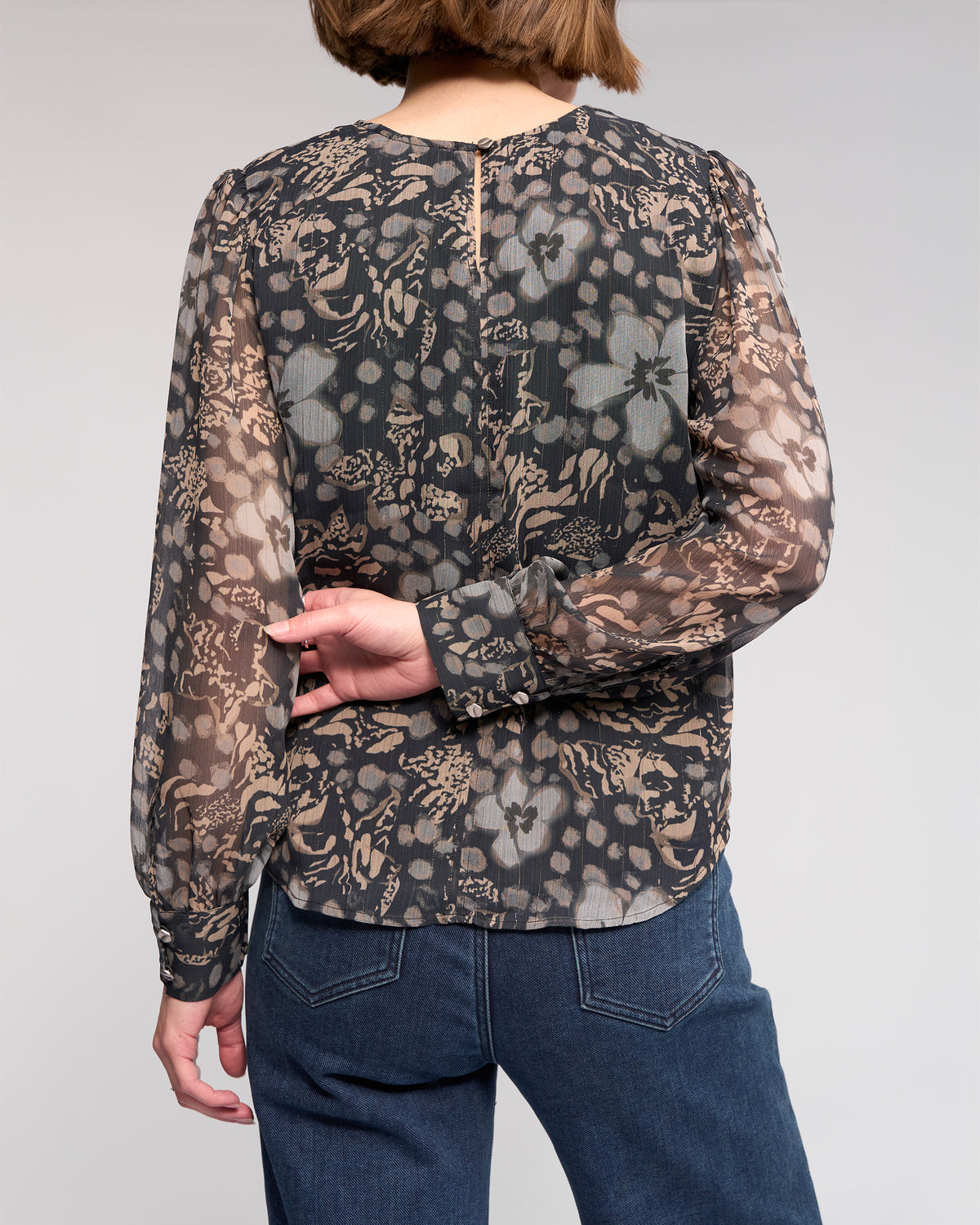A person stands with their back to the camera, wearing the Knewe Label Lexie Top - Hazy and blue jeans. One hand is behind their back, resting on their side.