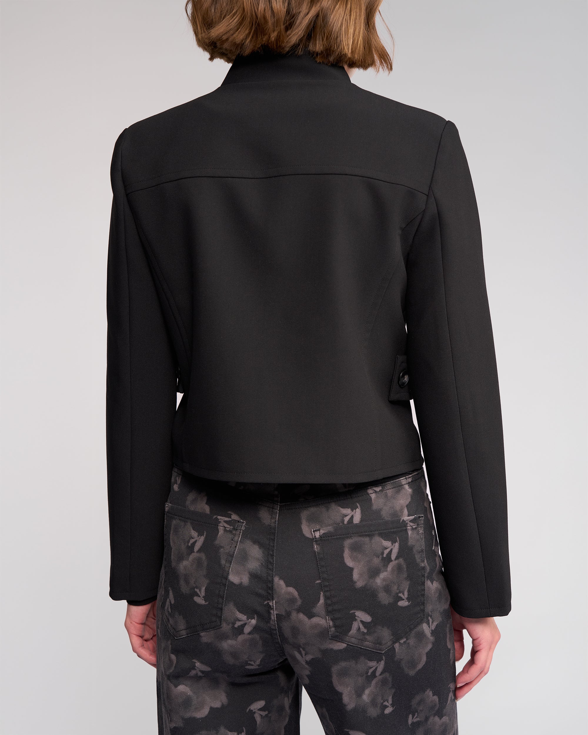 A person is shown from the back wearing the Knewe Label Soho Jacket in black and dark, gray floral jeans, against a plain light background.