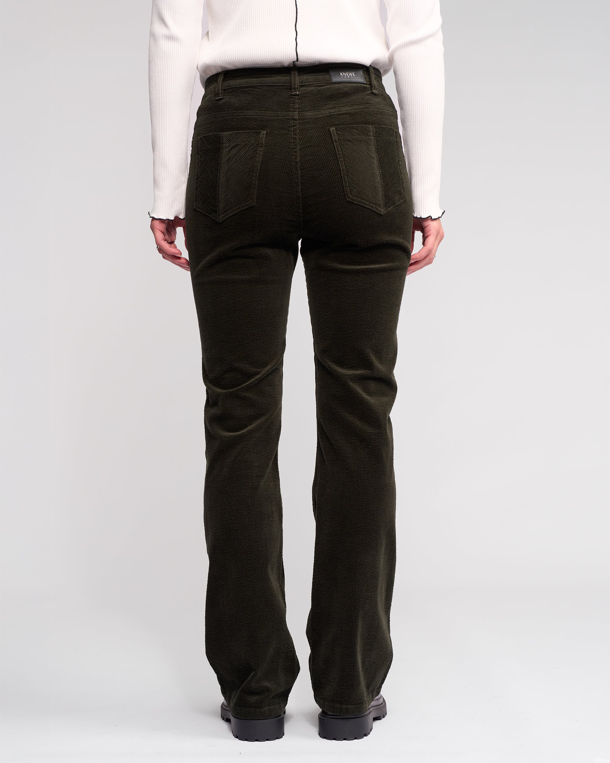 A person is seen from the back in Knewe Label's Potter Cord - Hunter wide-wale bootcut corduroy pants and a white long-sleeve top, standing against a plain light background.